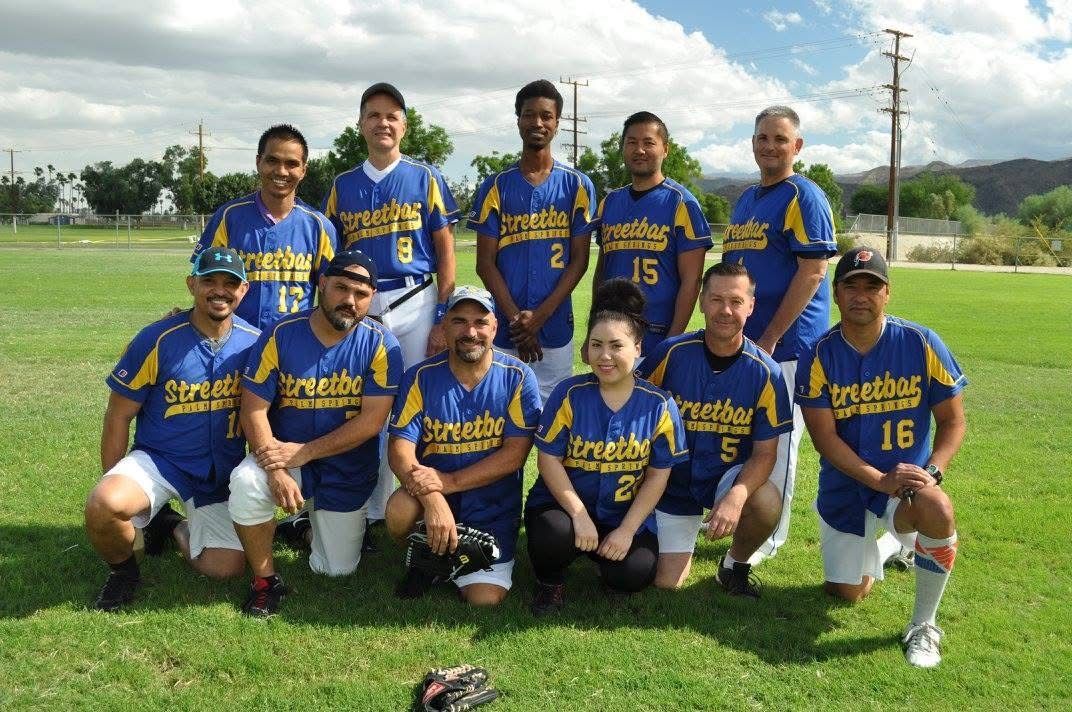 Baseball team in blue and yellow uniforms posing on a grassy field with gloves and bats