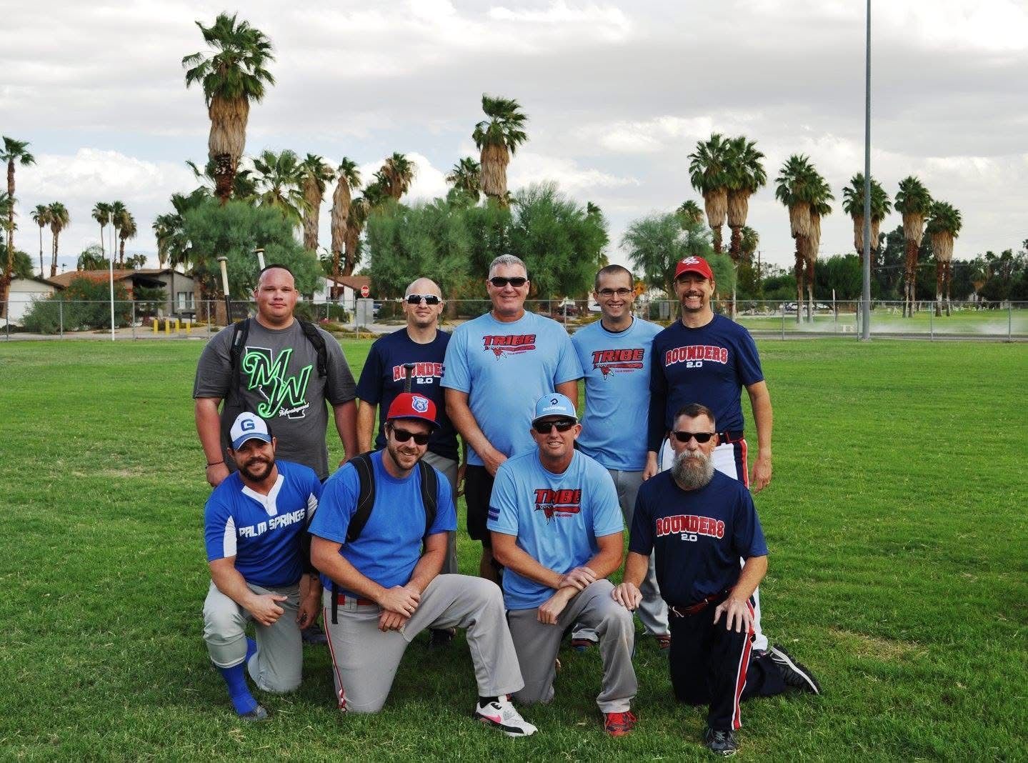 Group of people posing on a grassy field with palm trees in the background.