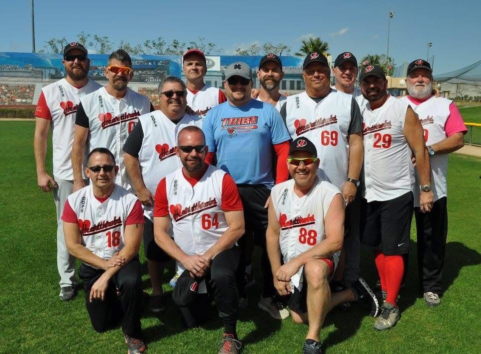 Baseball team posing outdoors on a sunny field, wearing white and blue uniforms.