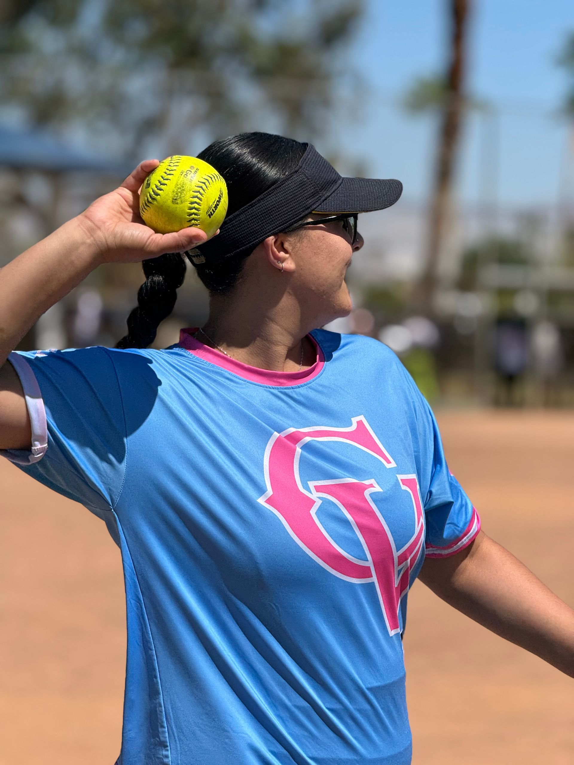 Softball player in blue jersey mid-throw on a sunny field