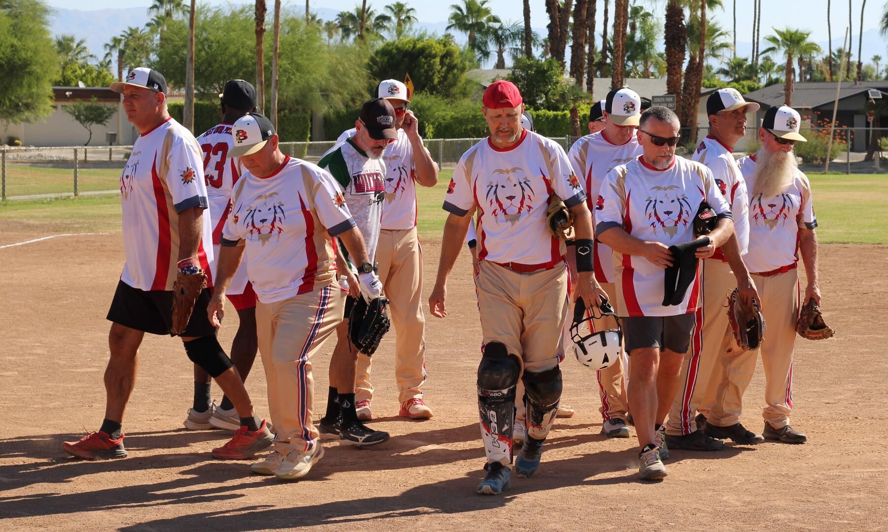Baseball team in white and red uniforms walking on a dirt field under bright sun