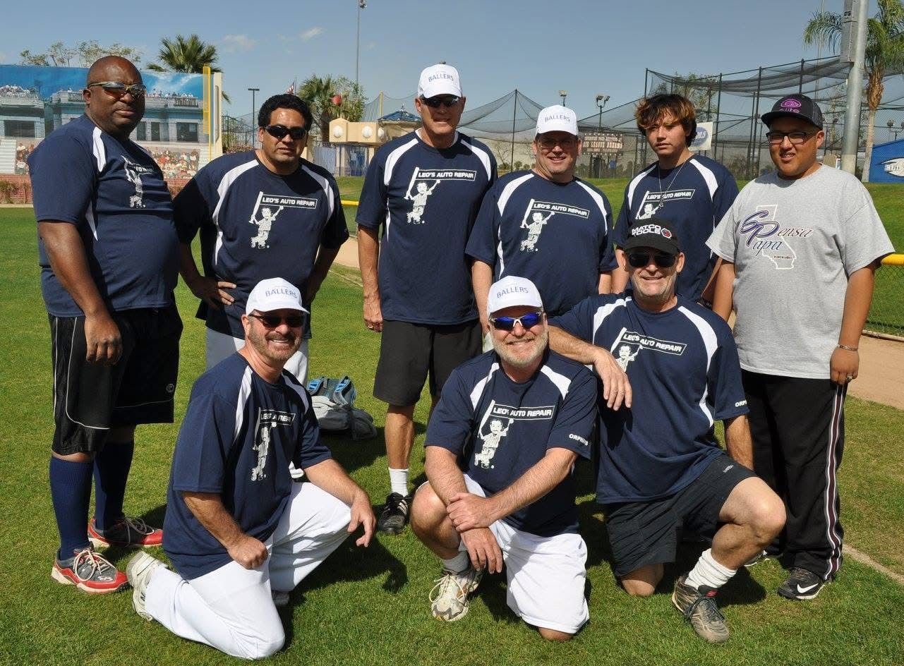 Baseball team posing outdoors on grass, wearing matching navy jerseys and caps