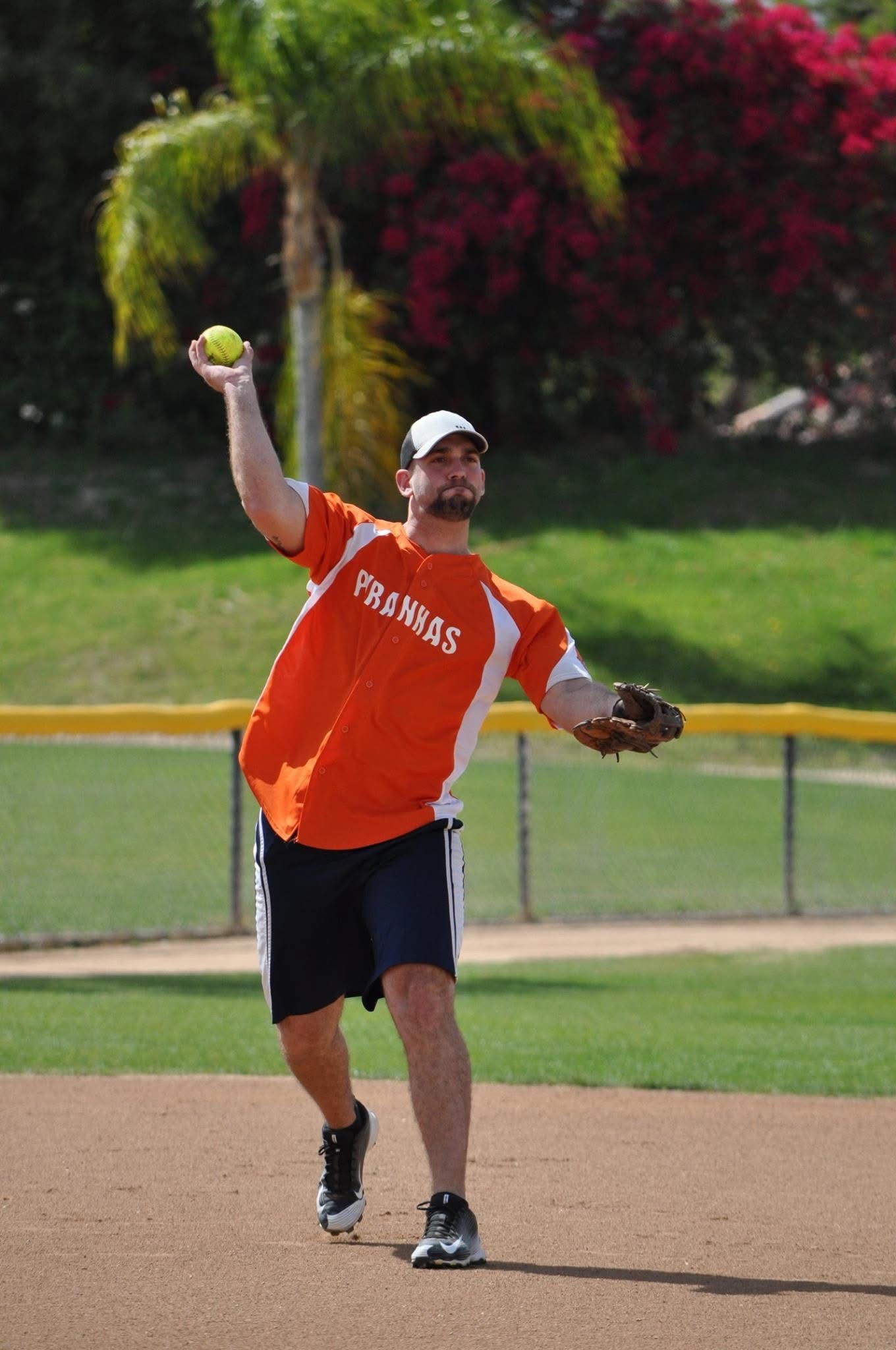 Softball player in orange jersey throwing a ball on a dirt field