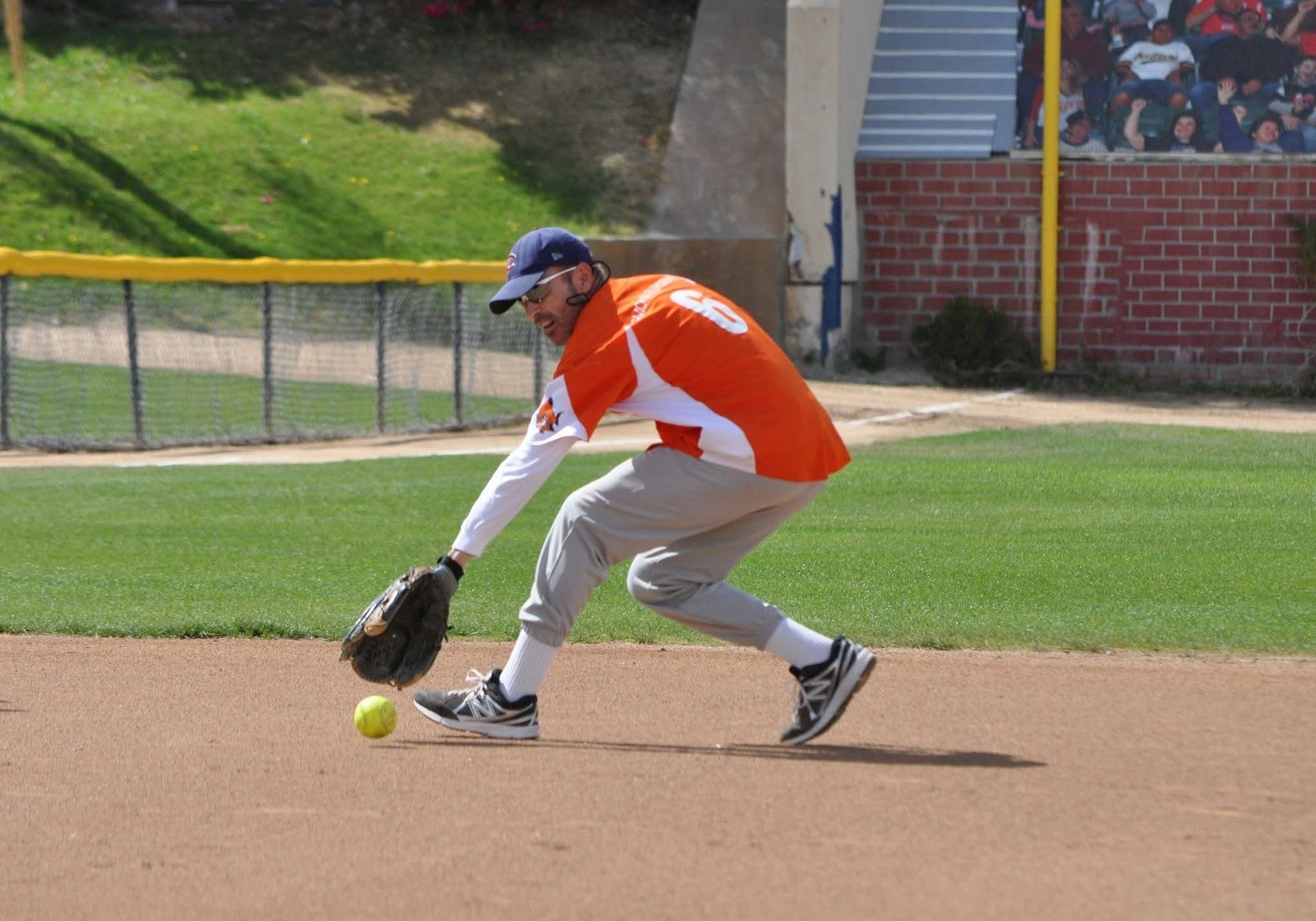 Baseball player in orange jersey fielding a ground ball on a dirt infield