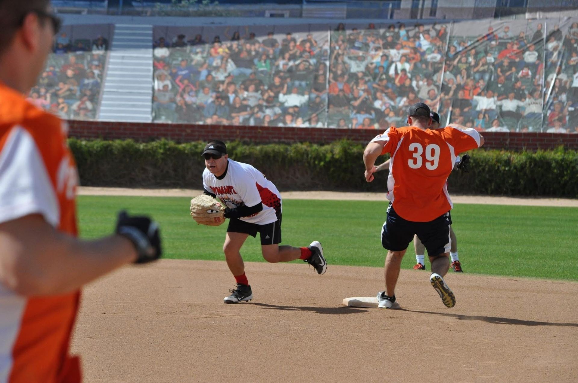 Two softball players in action on a field, one in a red jersey running toward base and another fielding the ball.