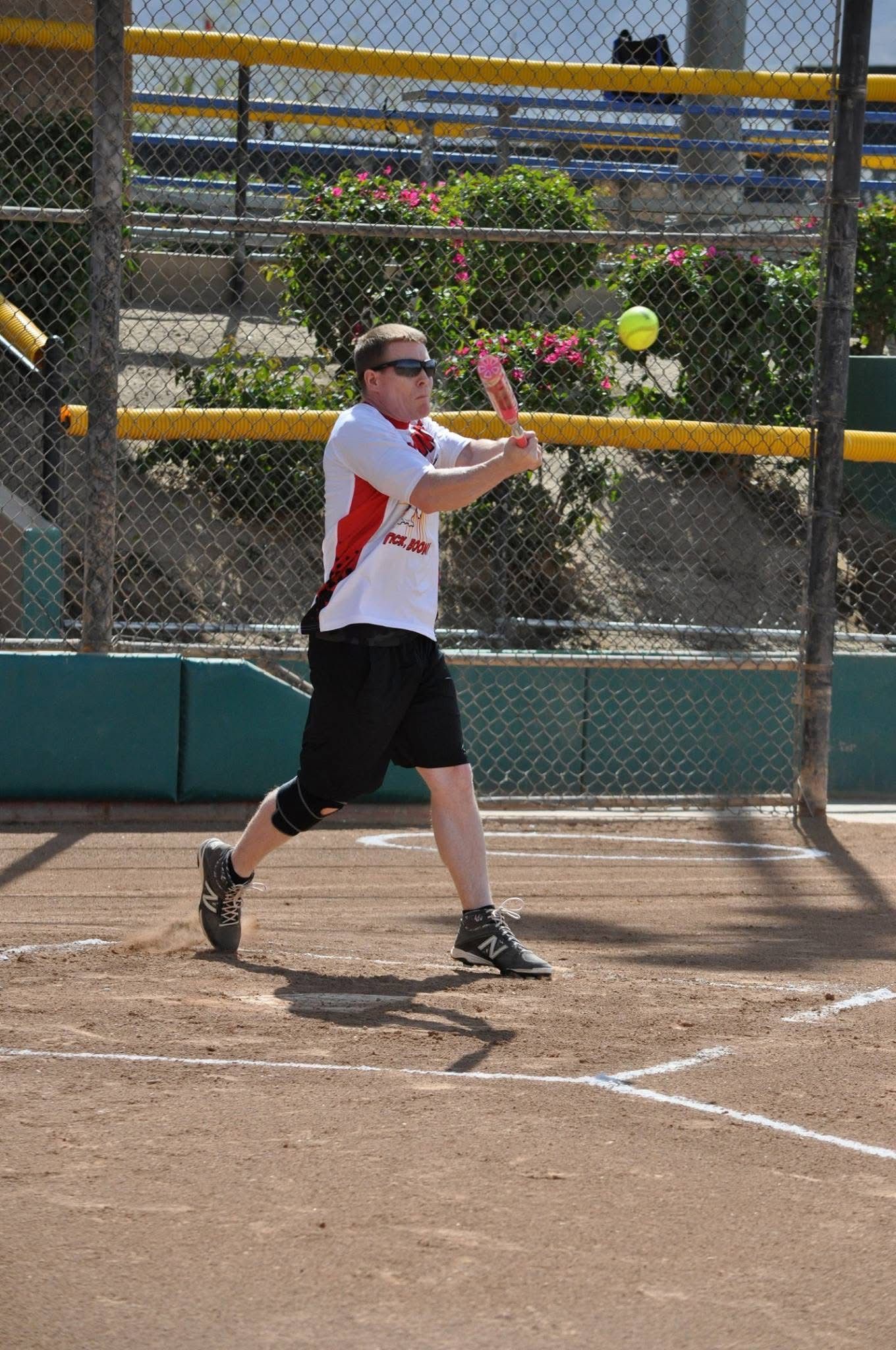 Softball player in white and red swings at a pitch on a dirt field.