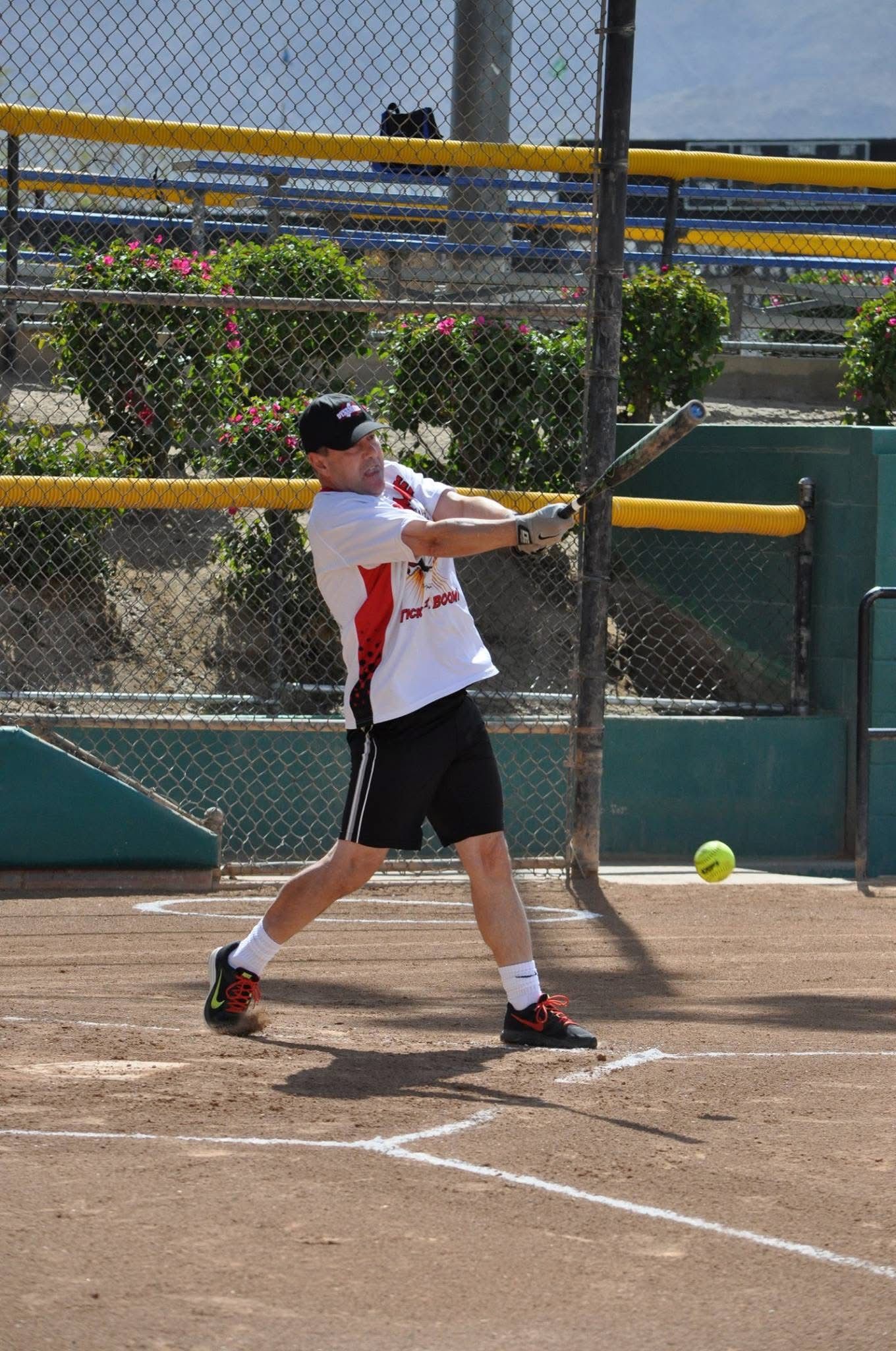 Softball batter swinging at a pitch on a dirt field near a chain-link fence and netting