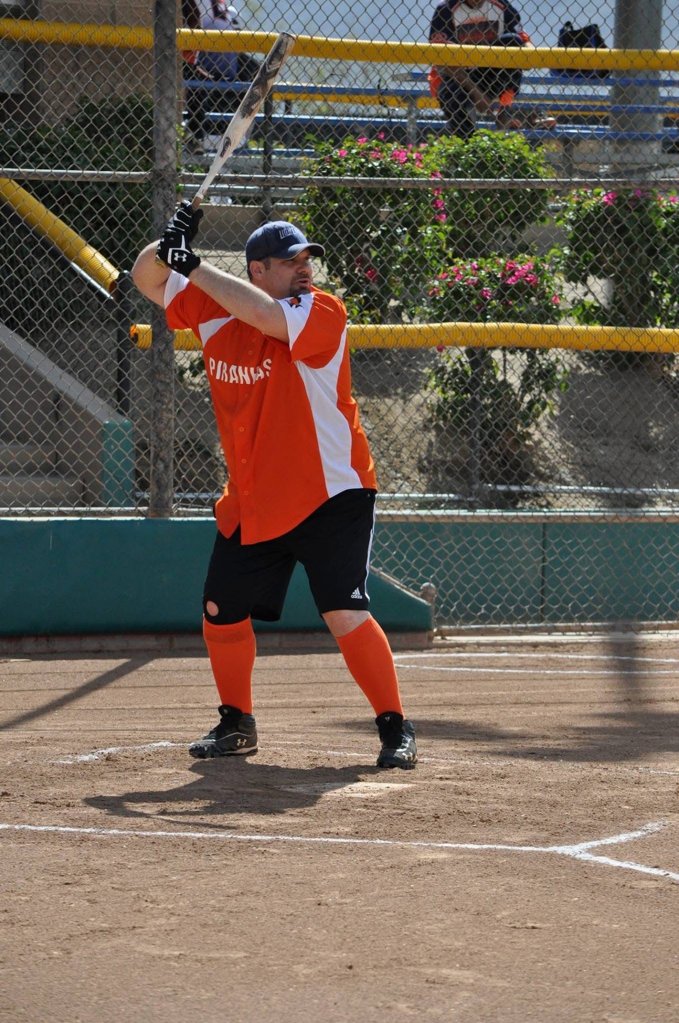 Softball batter in orange jersey and black helmet, ready to swing at home plate