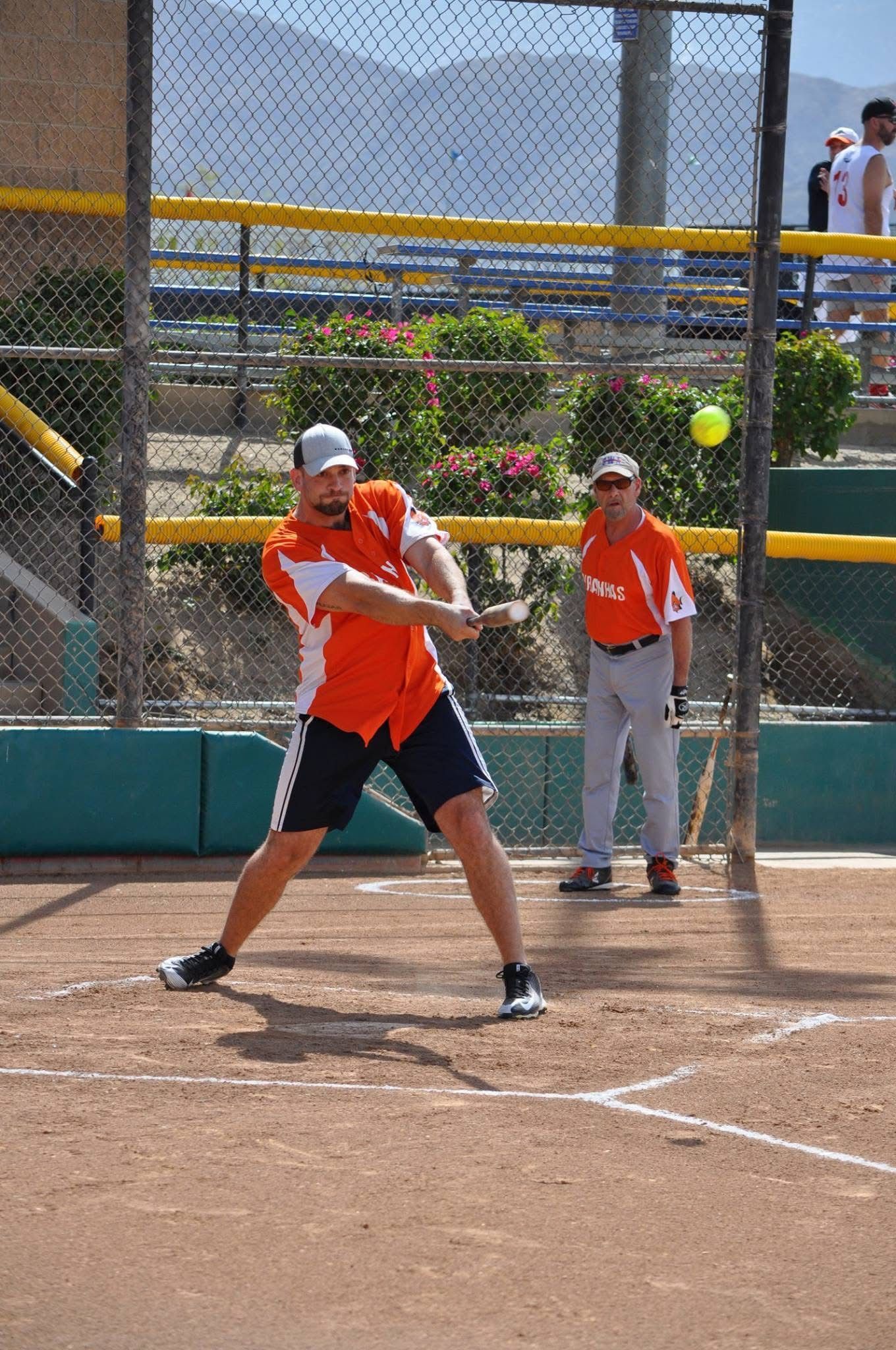 Softball batter in orange swings at a pitch while catcher waits behind the plate.