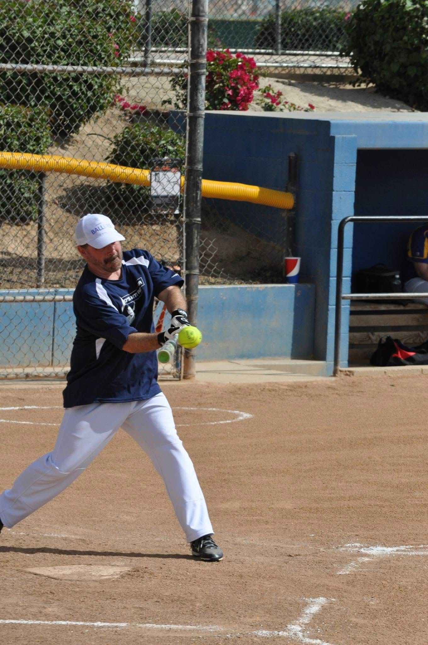 Softball player in blue shirt and white pants swinging a bat on a dirt field