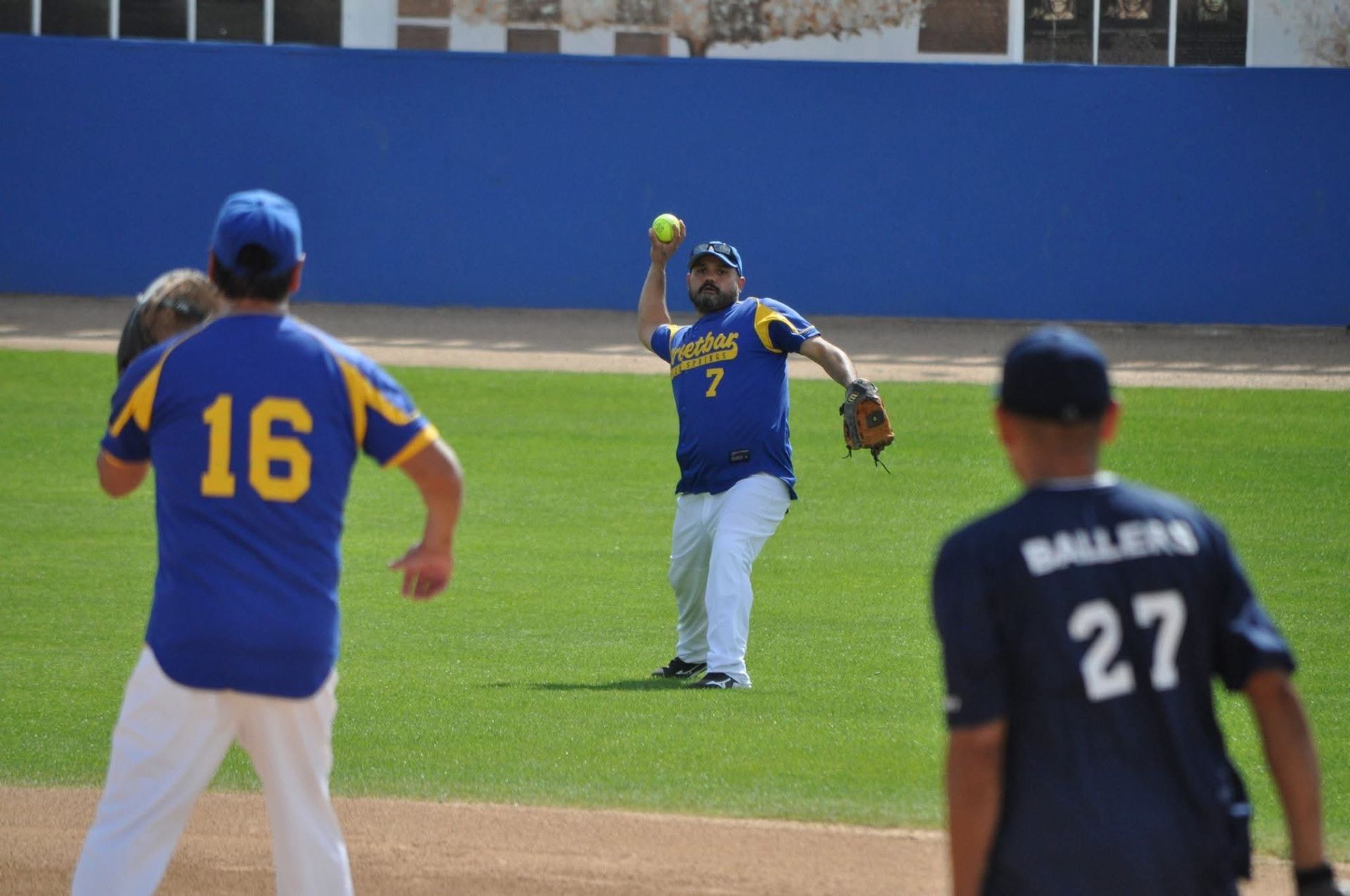 Three baseball players on the field, one in blue catching a ball near the outfield.