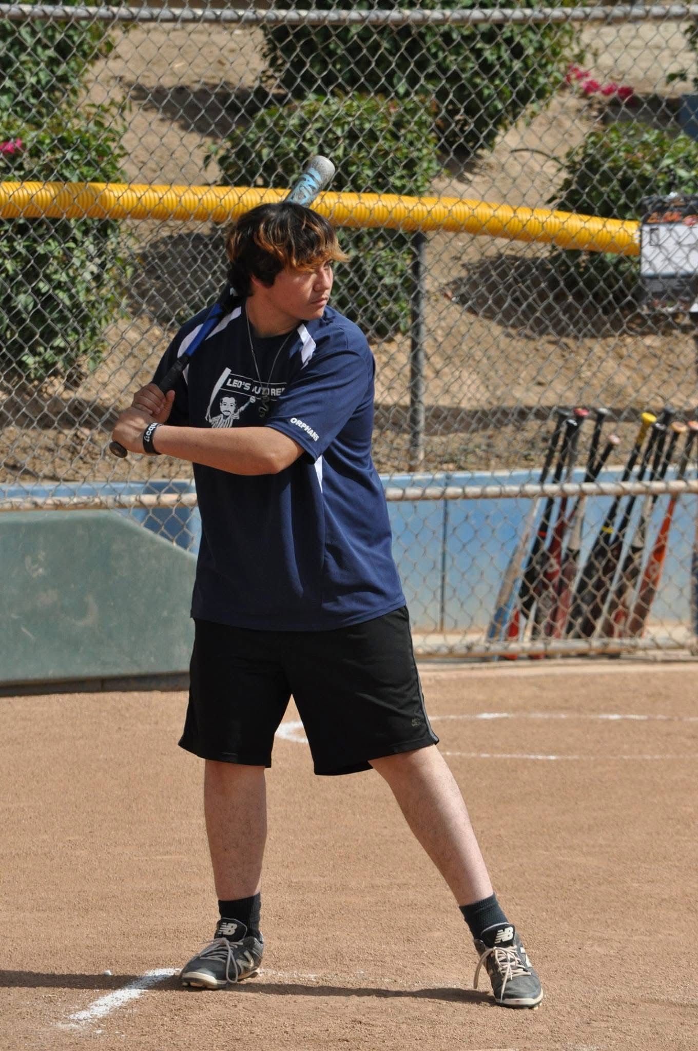 Baseball player in navy shirt and black shorts swings a bat on a field.