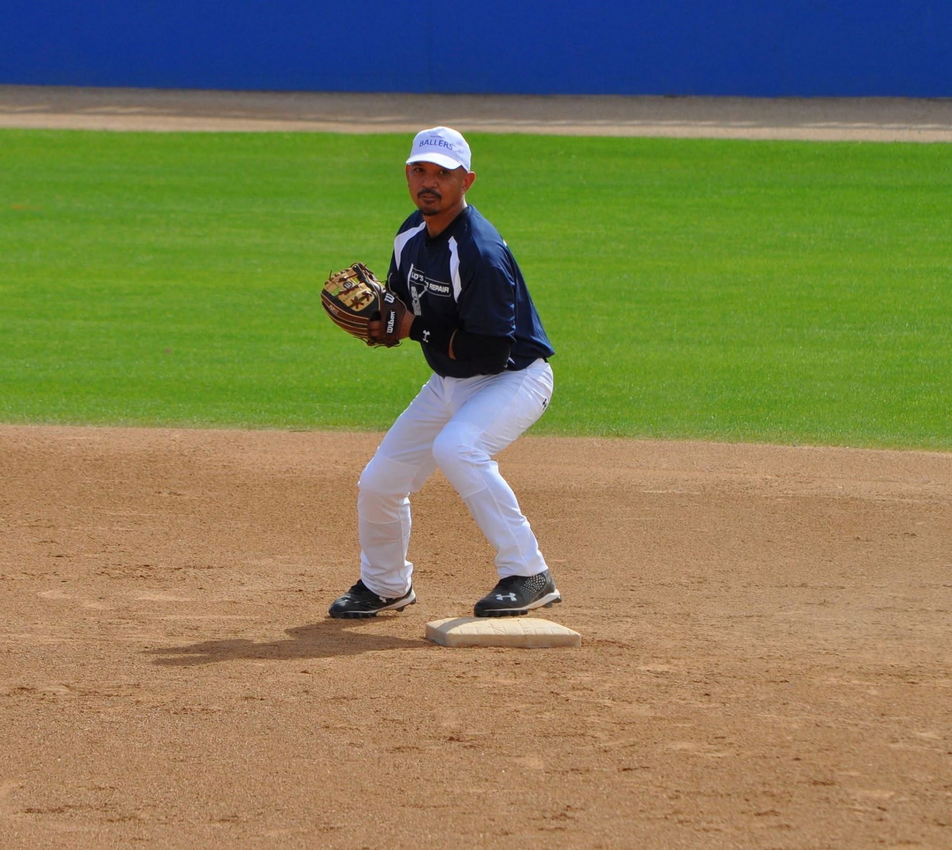 Baseball player in navy uniform ready to field a ground ball on the infield dirt.