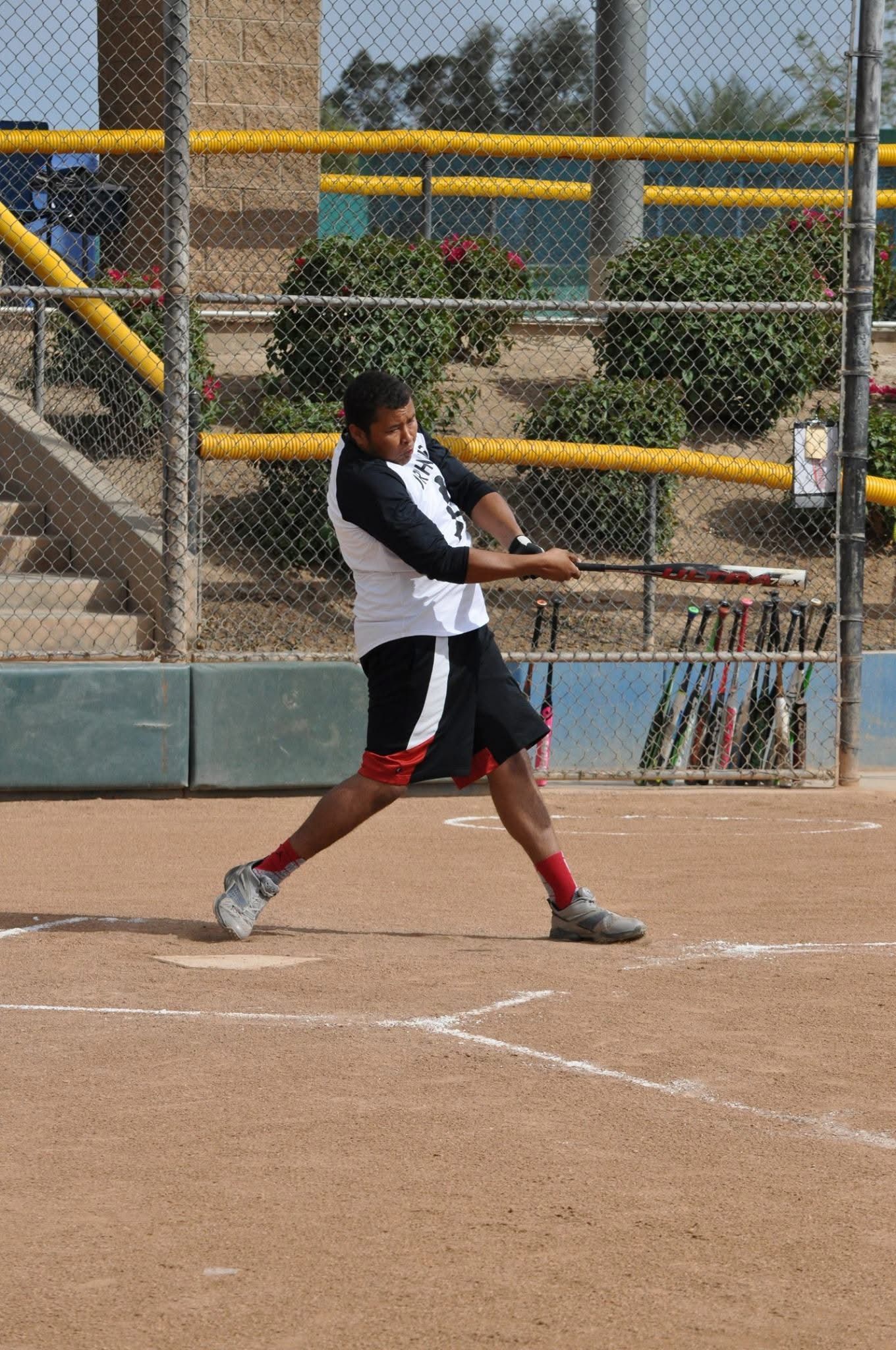 Softball player in black and white uniform swinging a bat on a dirt field