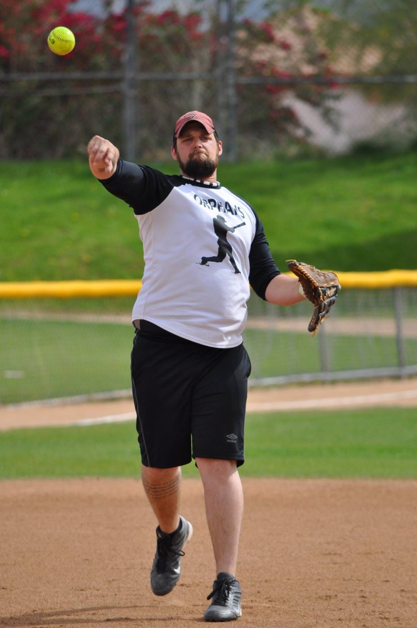 Softball player in white and black uniform throwing a pitch on a dirt field