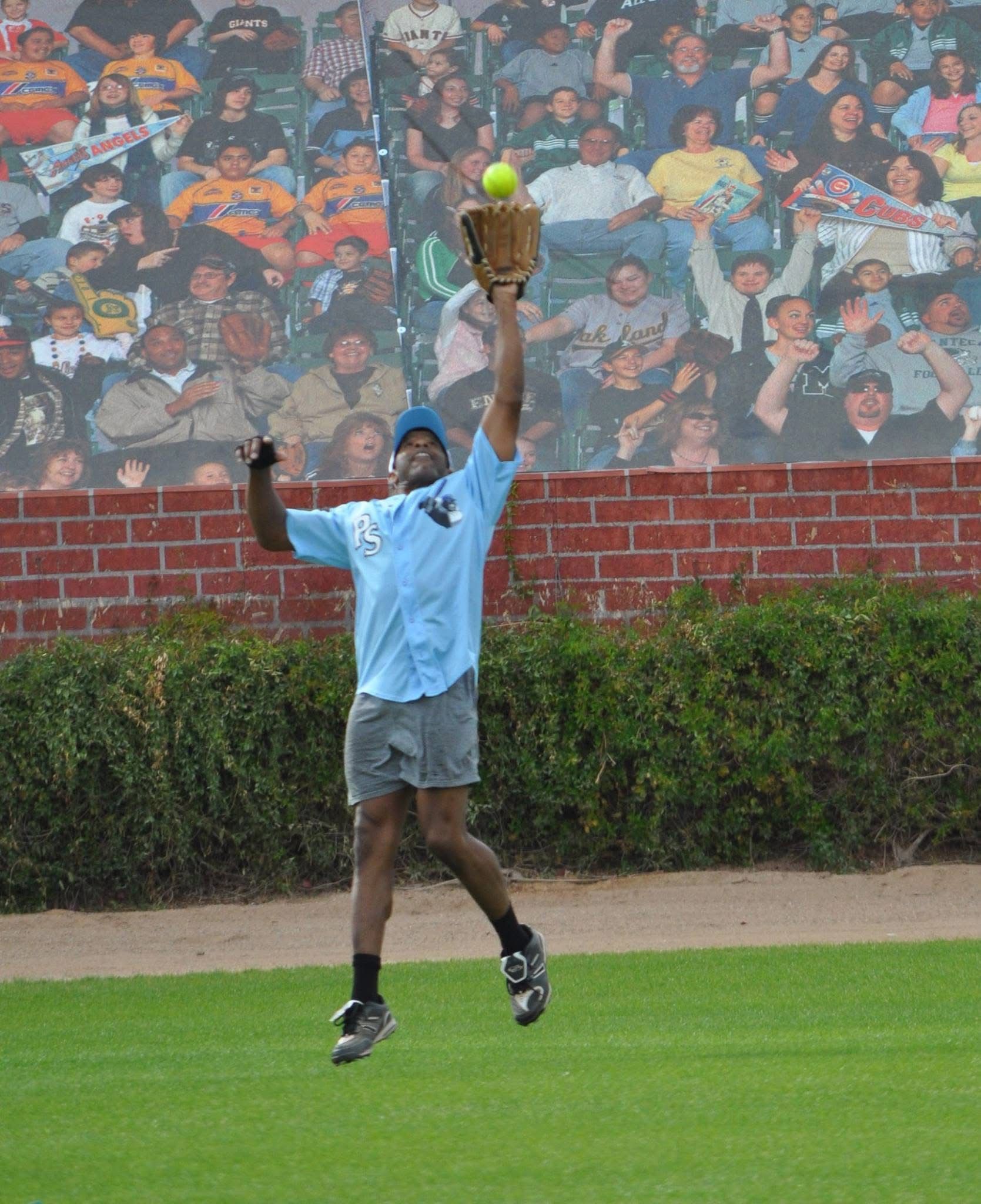 Tennis player leaps to catch a ball with an open racket on a grass court, crowd mural behind them