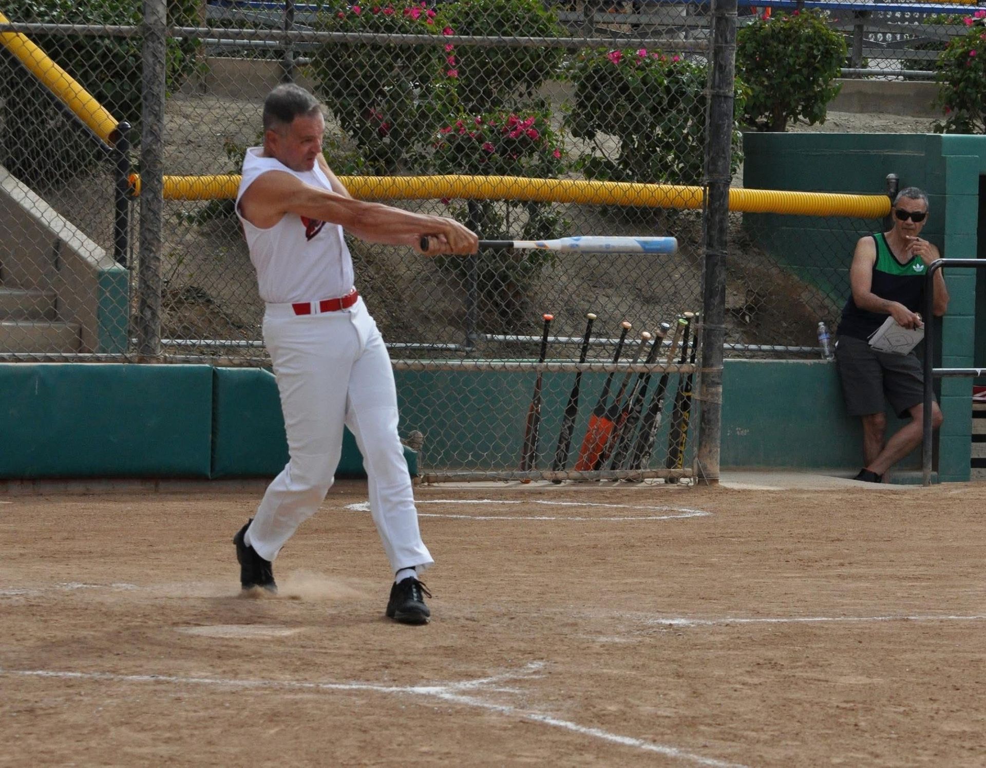 Baseball player in white uniform swinging a bat near home plate on a dusty field.