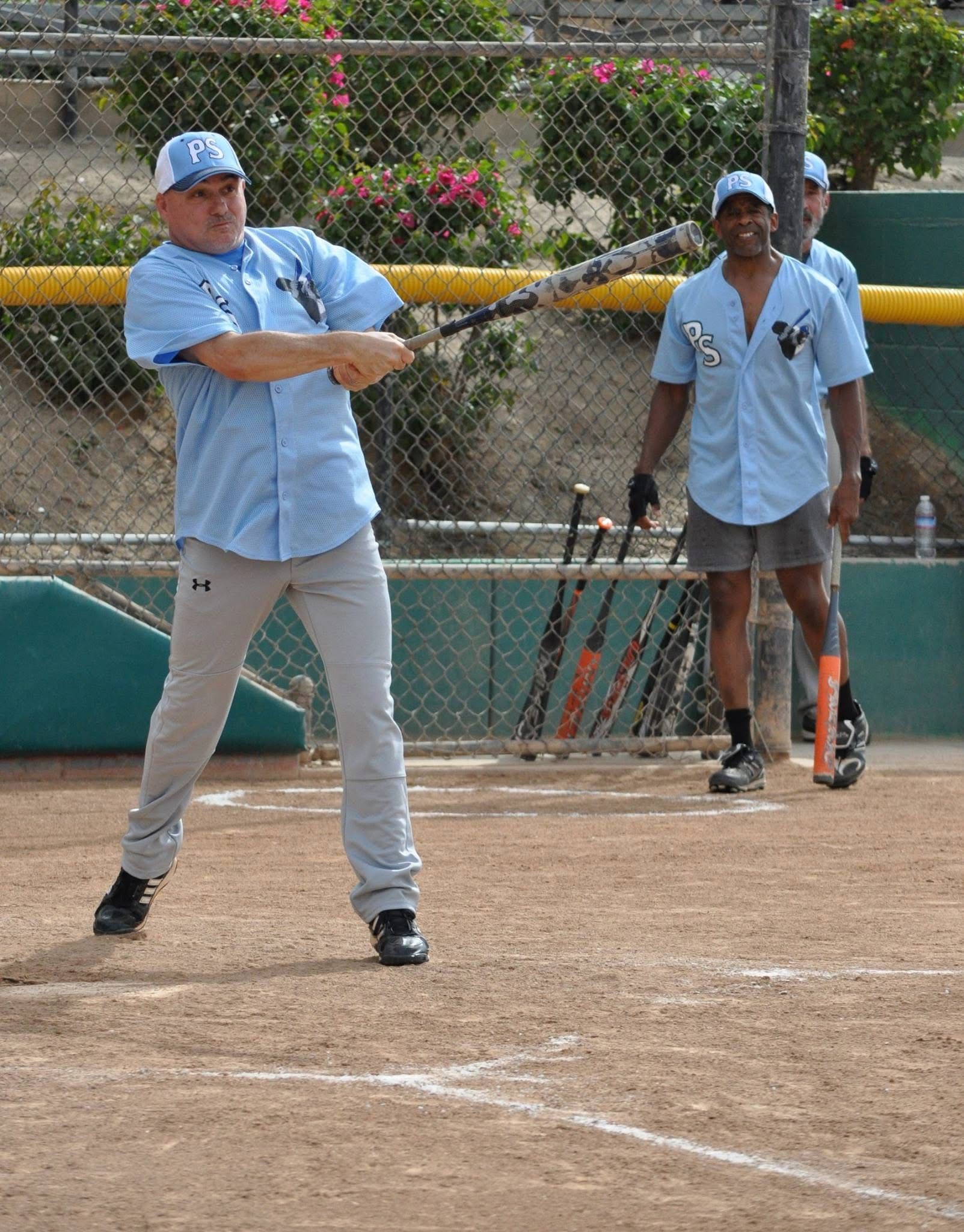 Baseball batter in light blue swings at a pitch, with umpire standing behind on the field.
