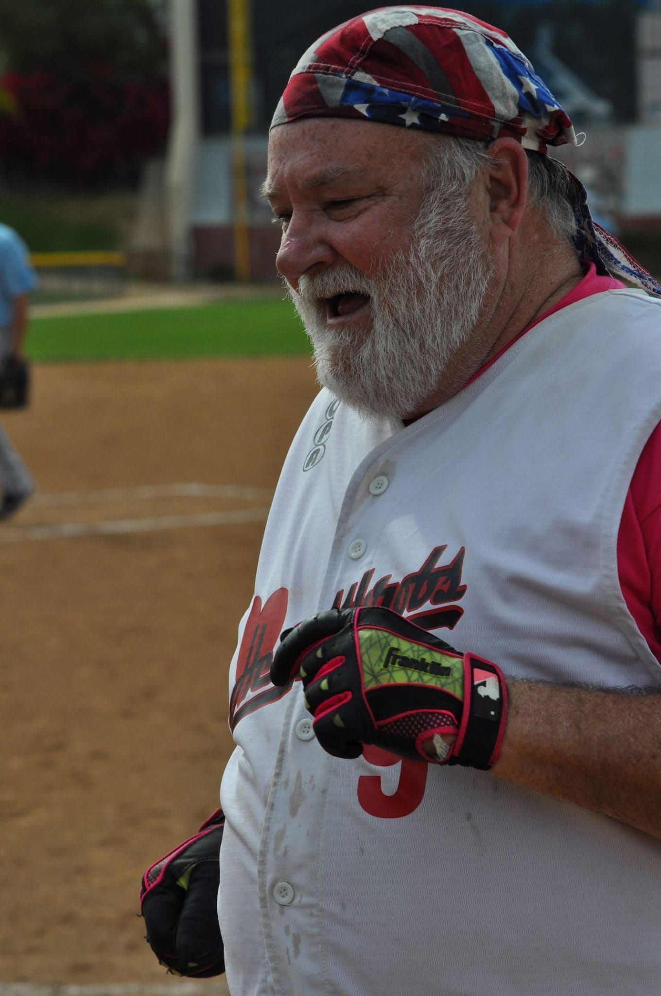 Baseball player in white jersey and red gloves standing on the field, wearing a red, white, and blue bandana.