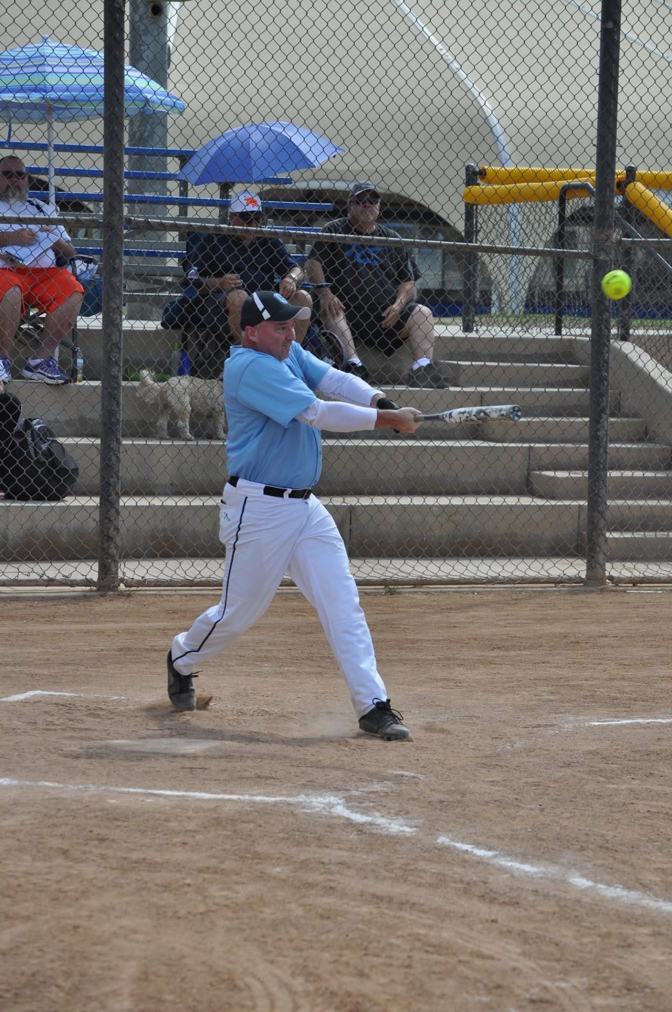 Baseball player in light blue uniform swinging a bat on a dirt field.