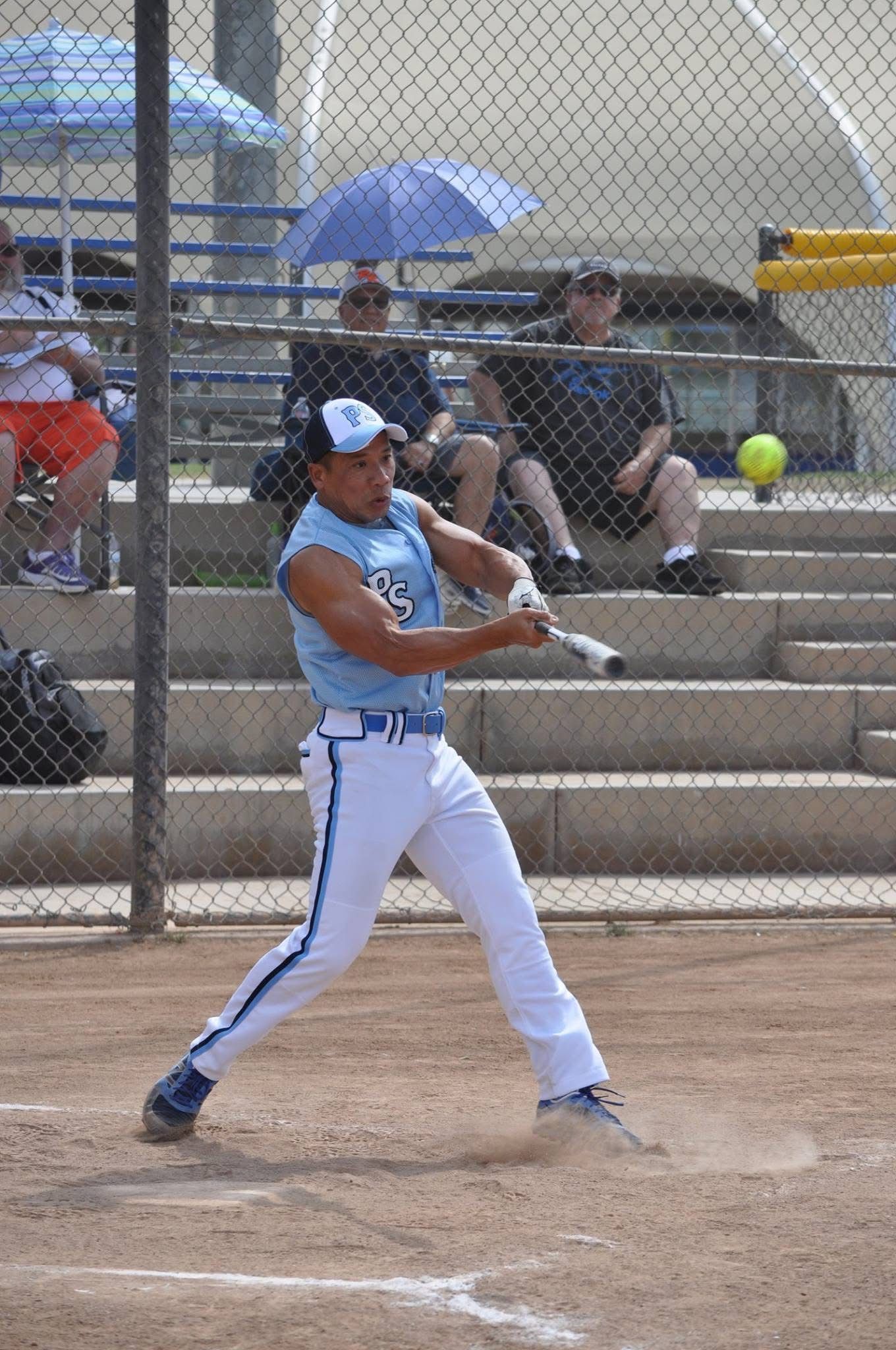 Softball batter in blue uniform swings at a pitch on a dirt field.