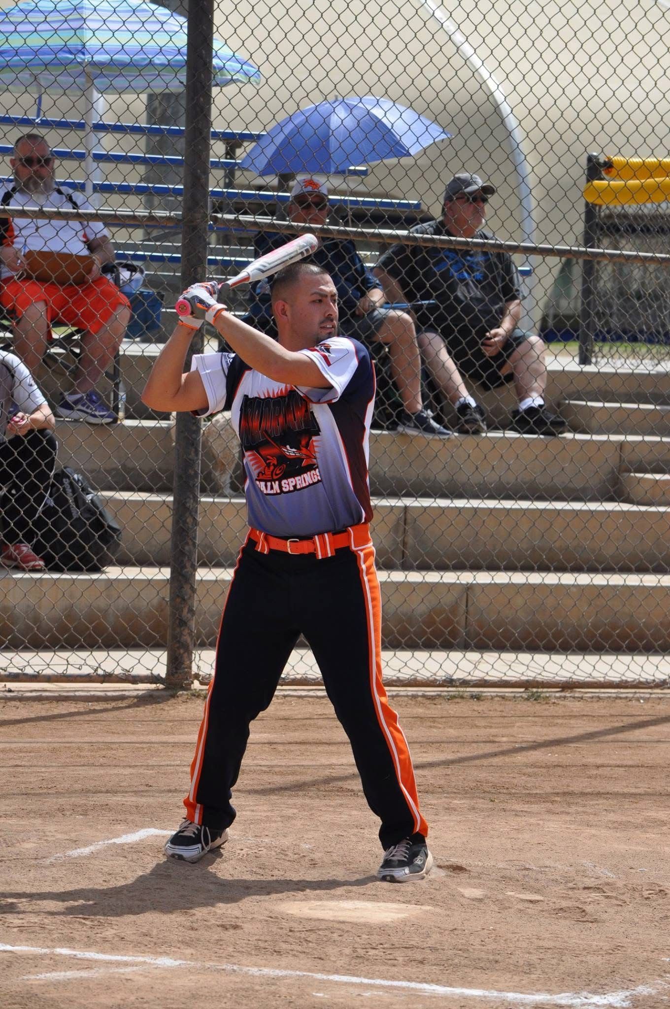 Softball batter in black and orange uniform preparing to swing at home plate