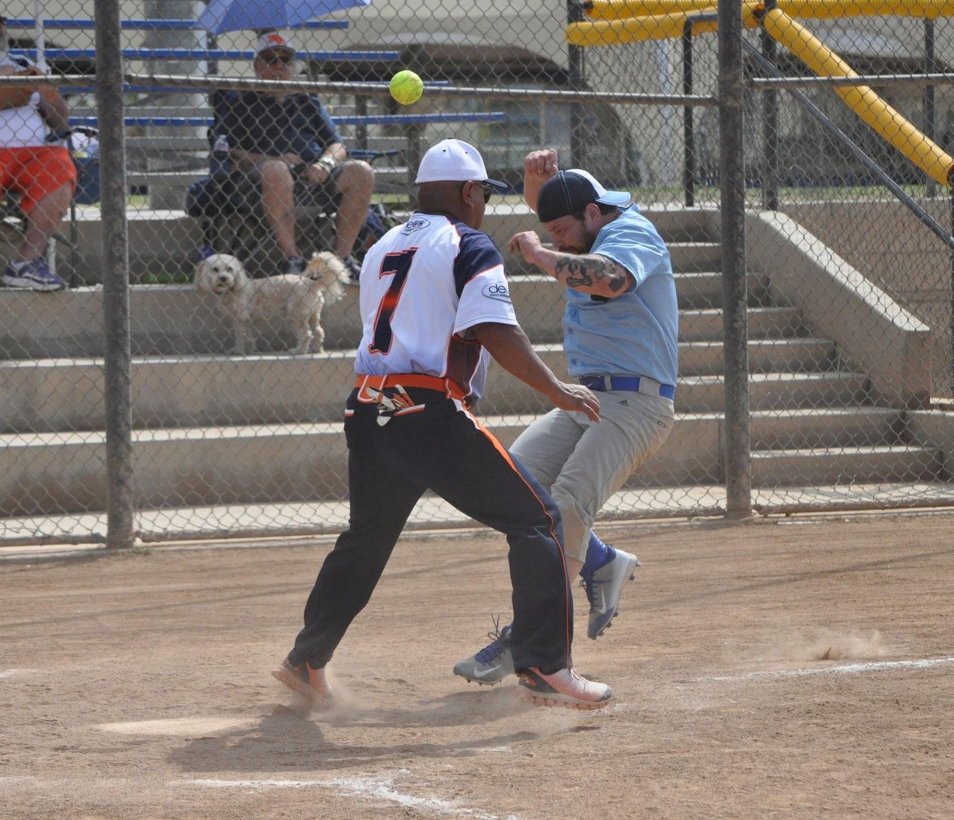 Two baseball players in gray and white uniforms collide near the base on a dirt field.