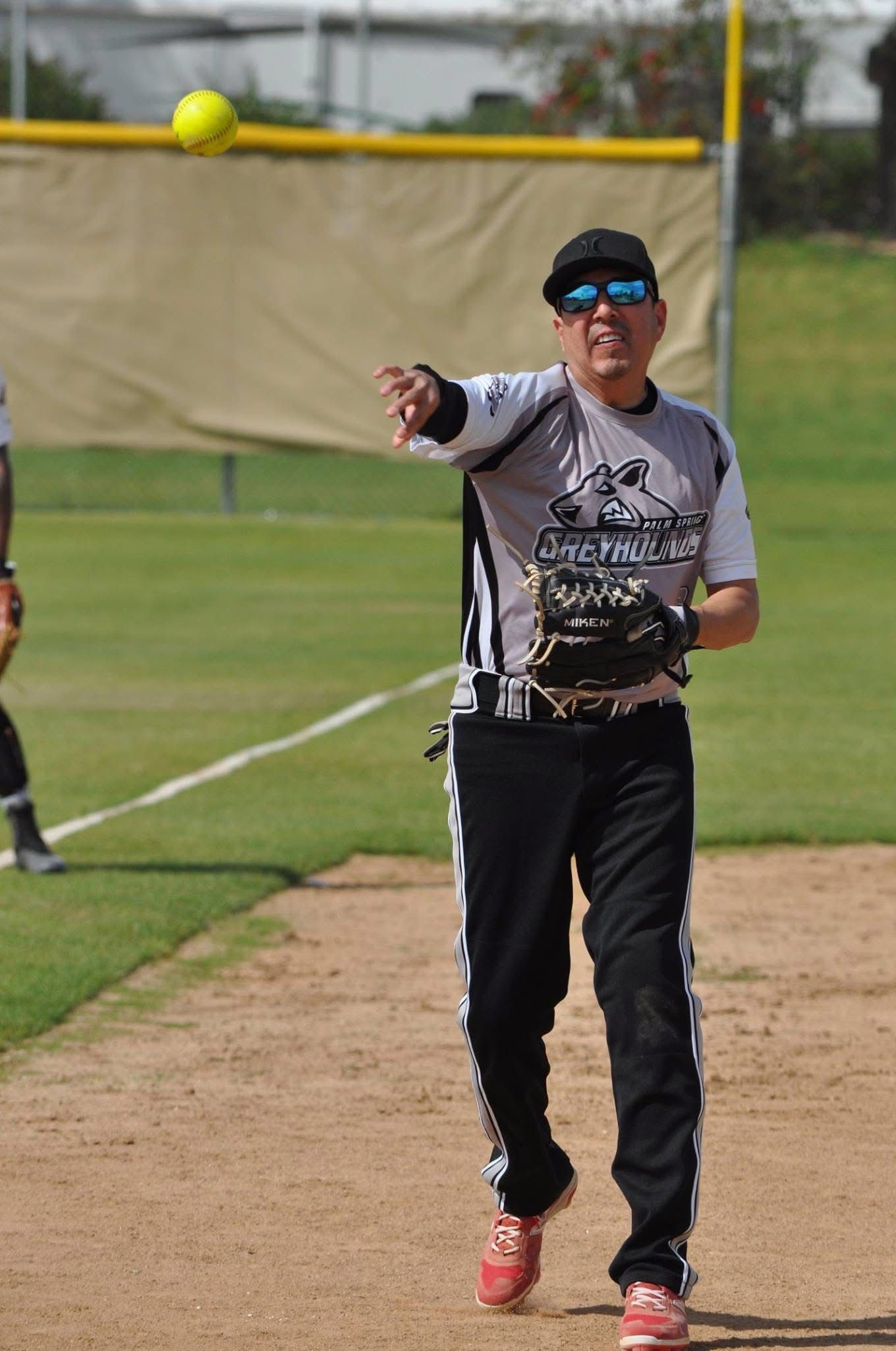Softball player in gray and black uniform throwing a yellow ball on a field