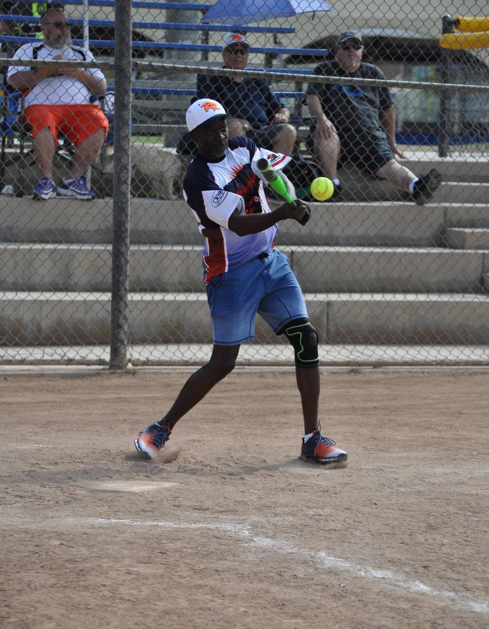 Softball player in white and blue uniform swings at a pitched ball on a dirt field.