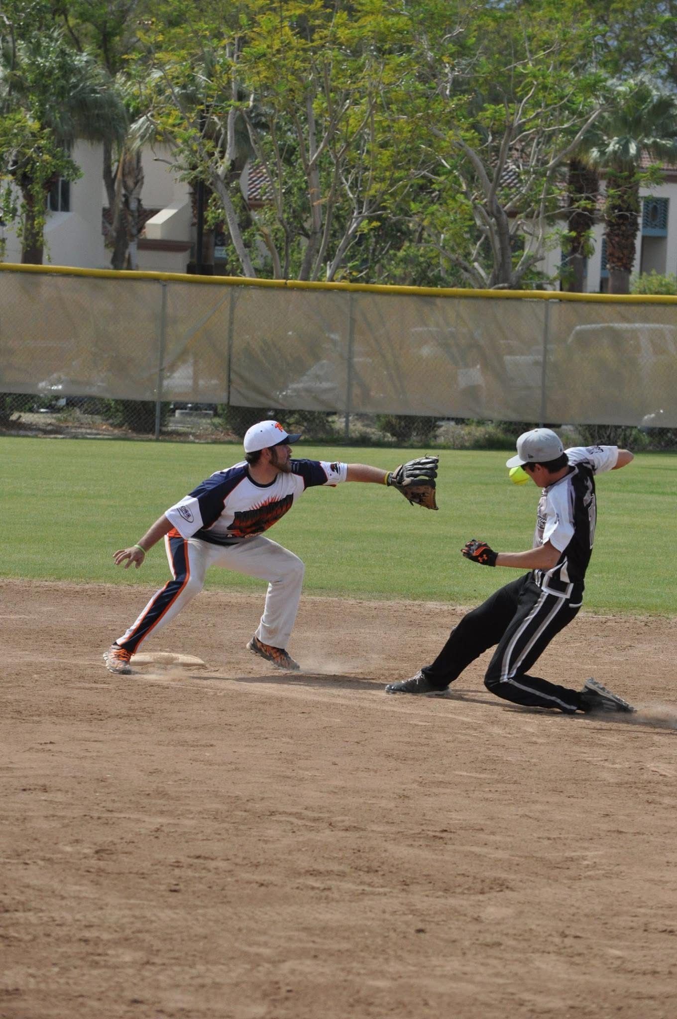 Two baseball players mid-play on a dirt infield, one reaching to tag the other near a base.