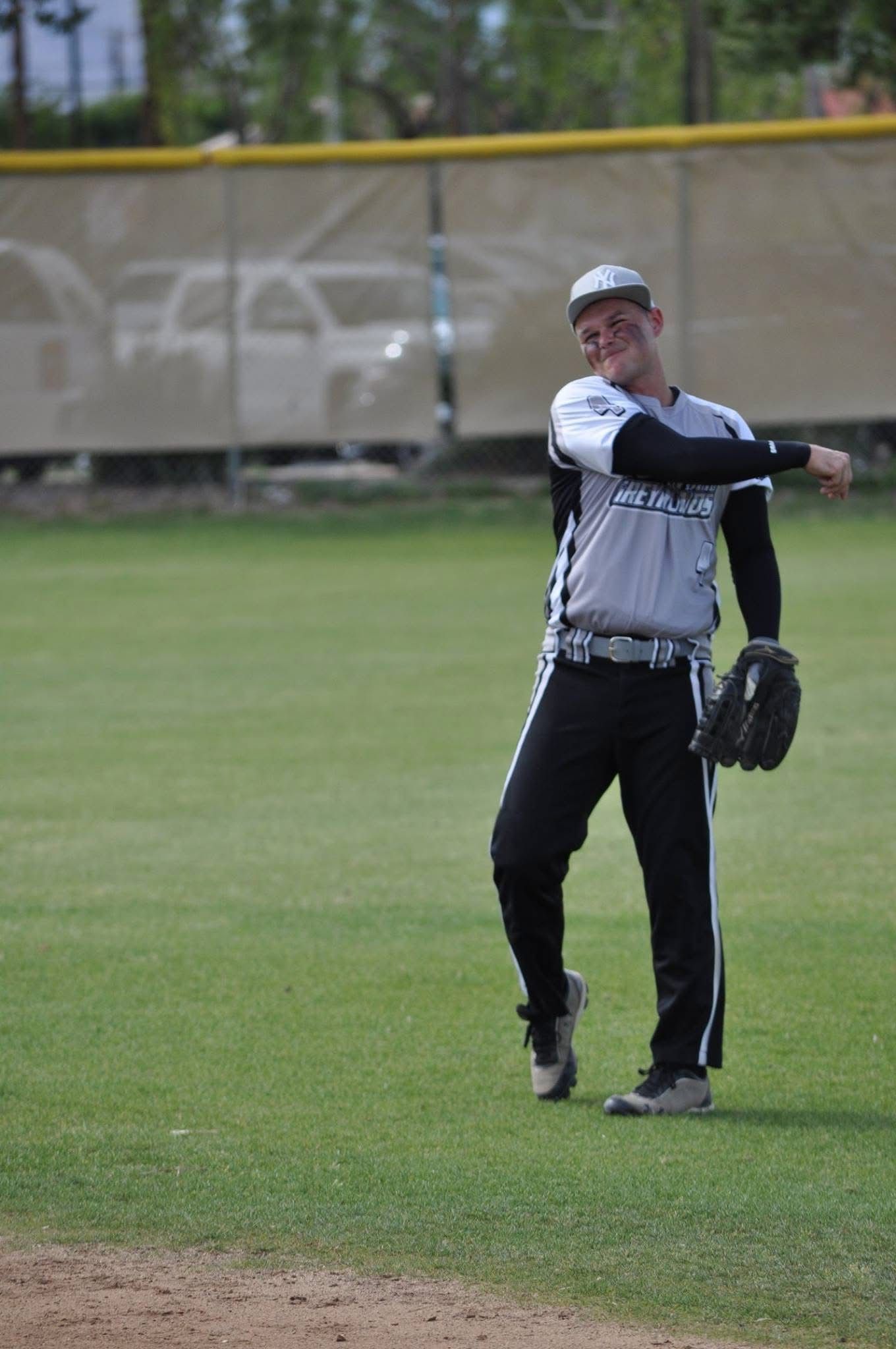Baseball player in white and black uniform standing on the field with a glove, pointing to the side.
