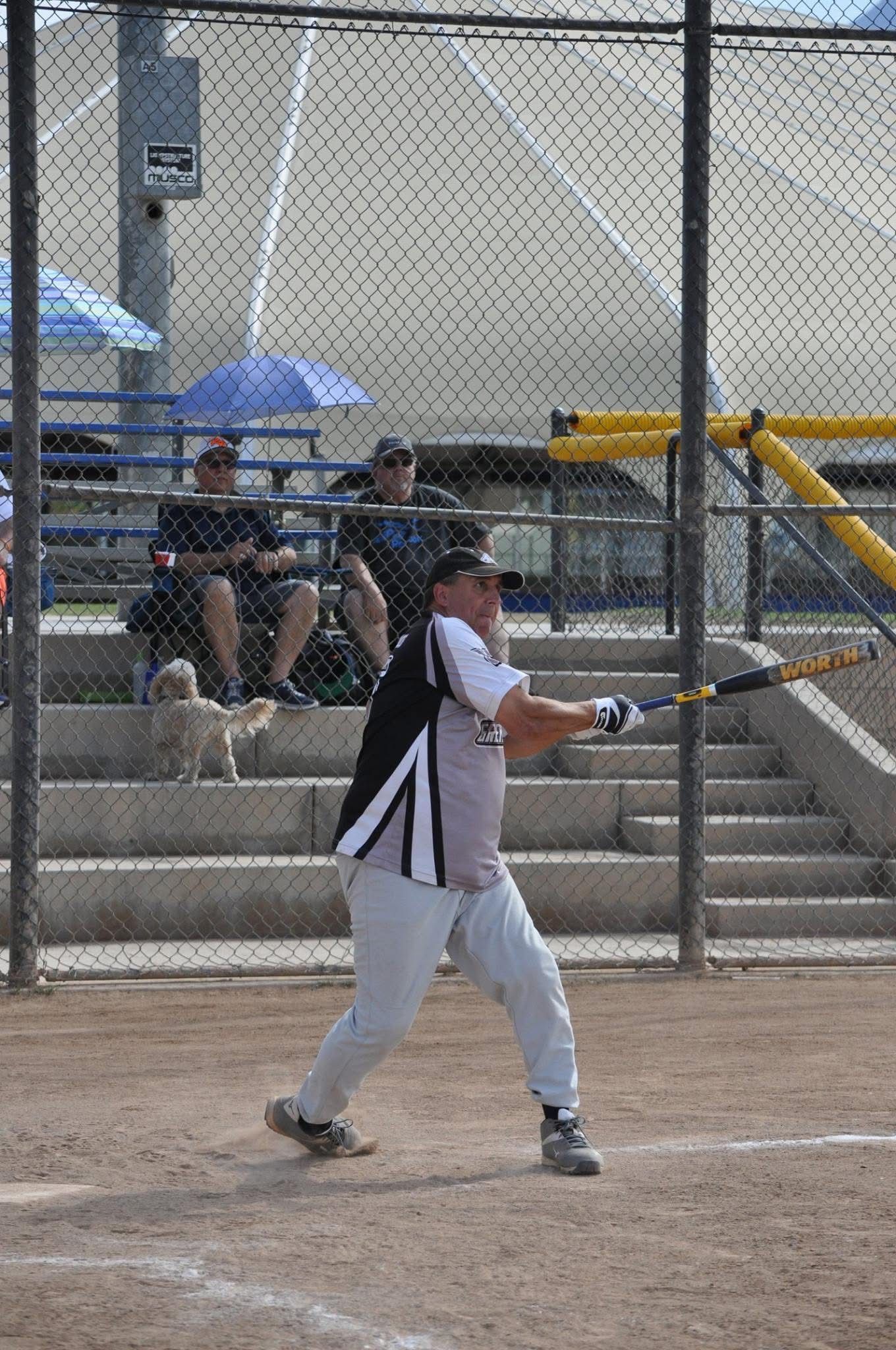 Baseball player in white uniform swinging a bat at home plate on a dusty field.
