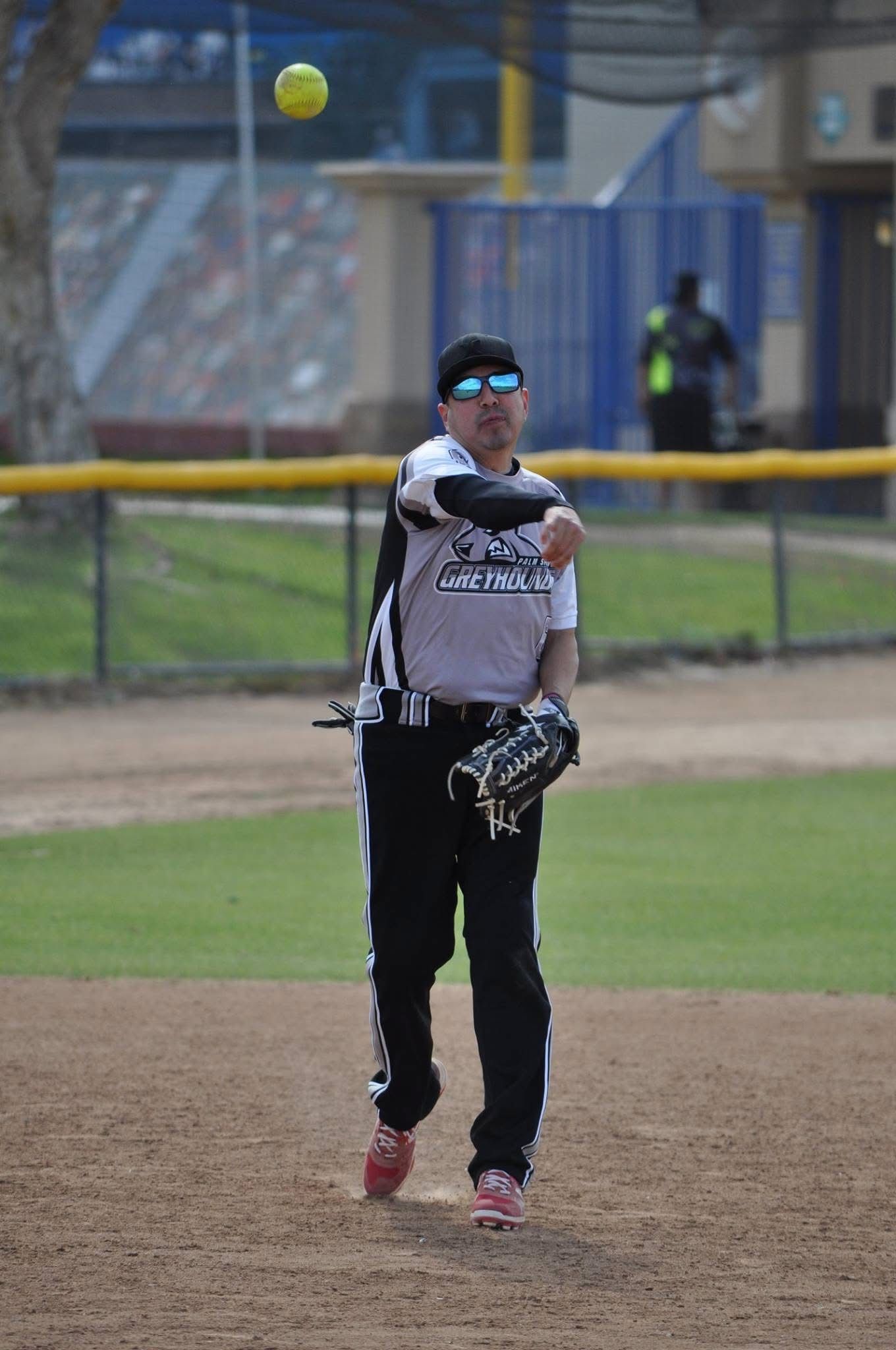 Softball player in gray jersey and black pants throws a ball on a dirt field.