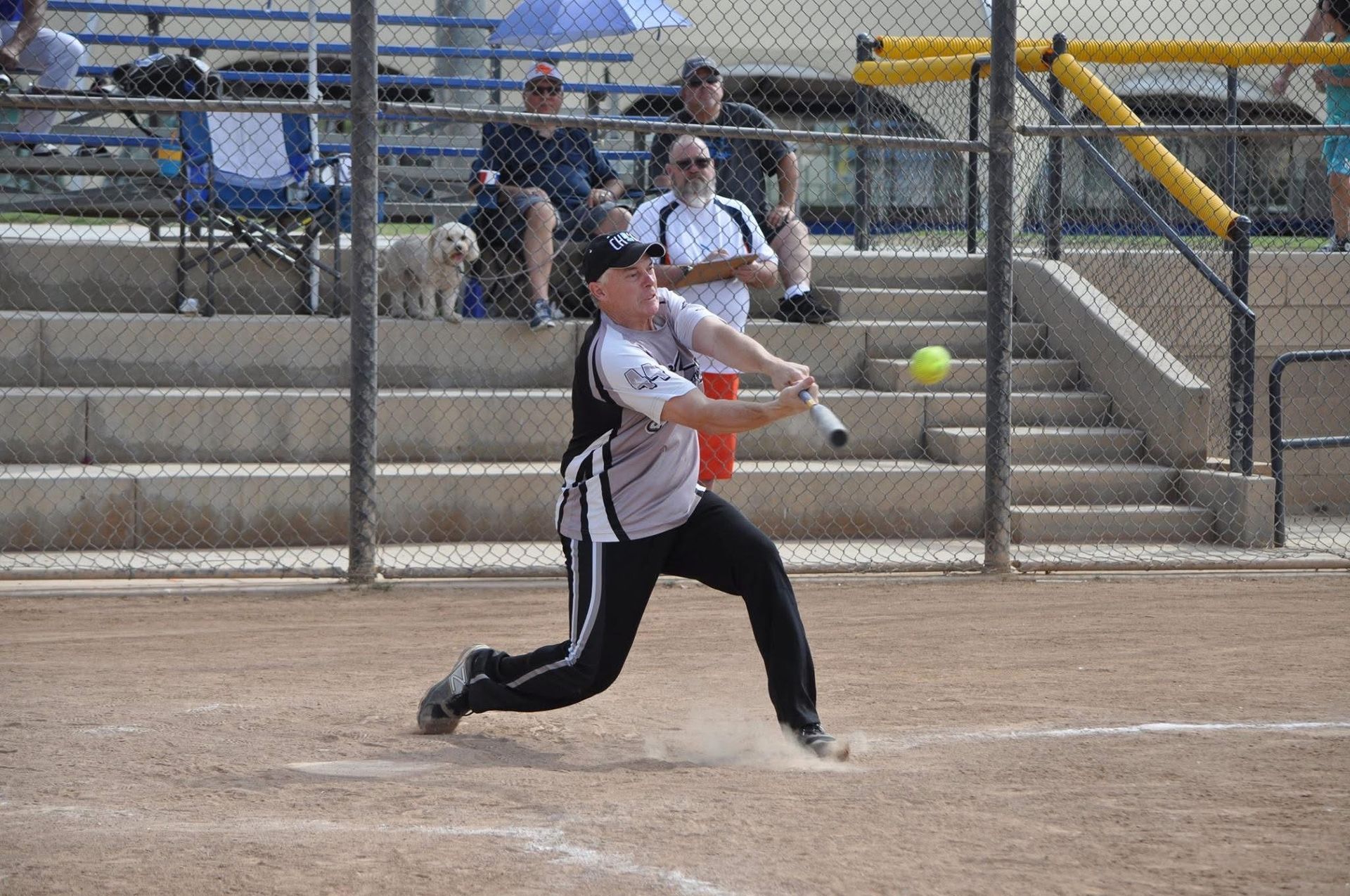 Softball player in black and white uniform swinging a bat on a dirt field
