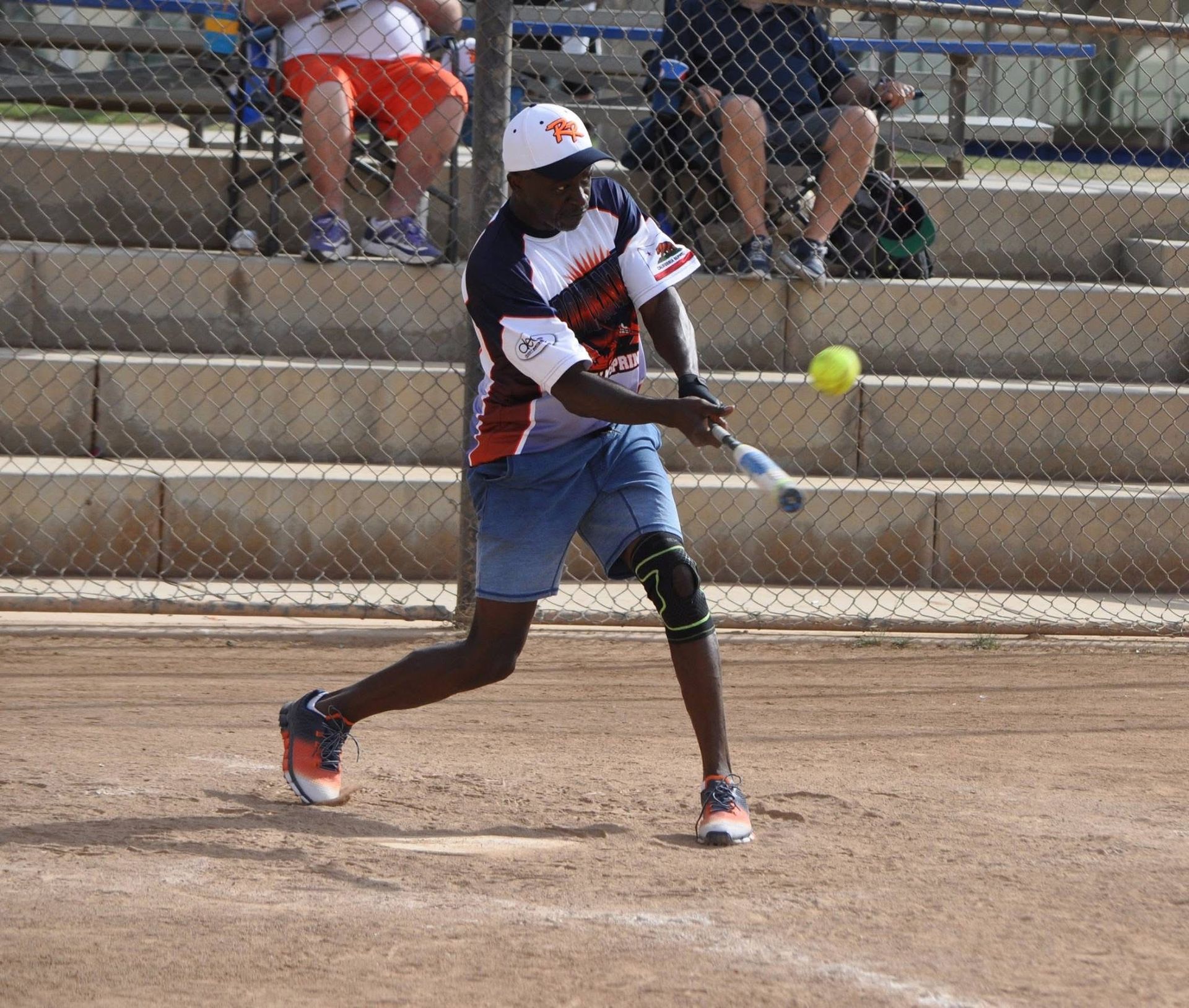 Softball player in white and red uniform swings at a ball on a dirt field