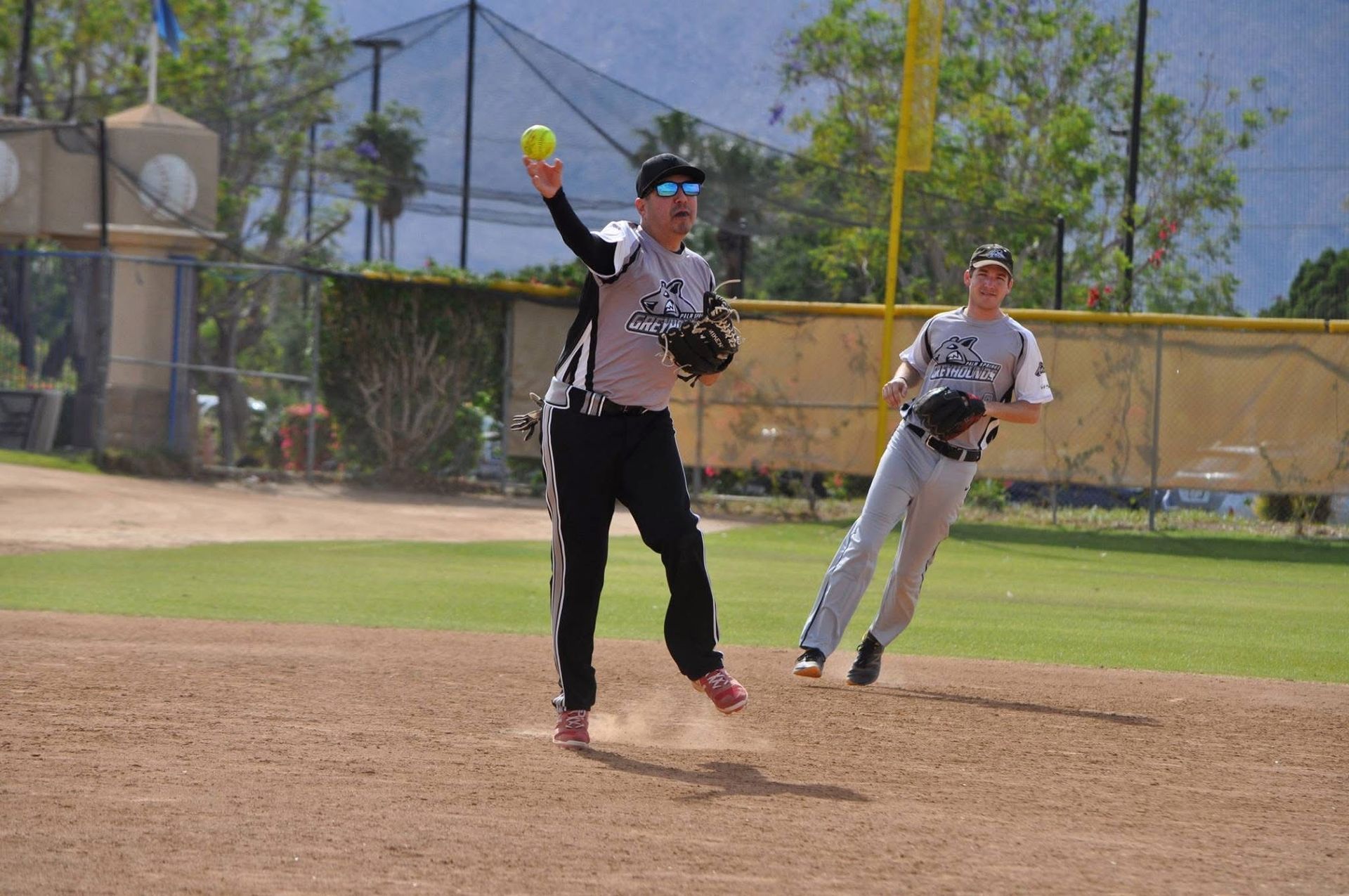 Two baseball players near a base, one reaching for a ball on a sunny field