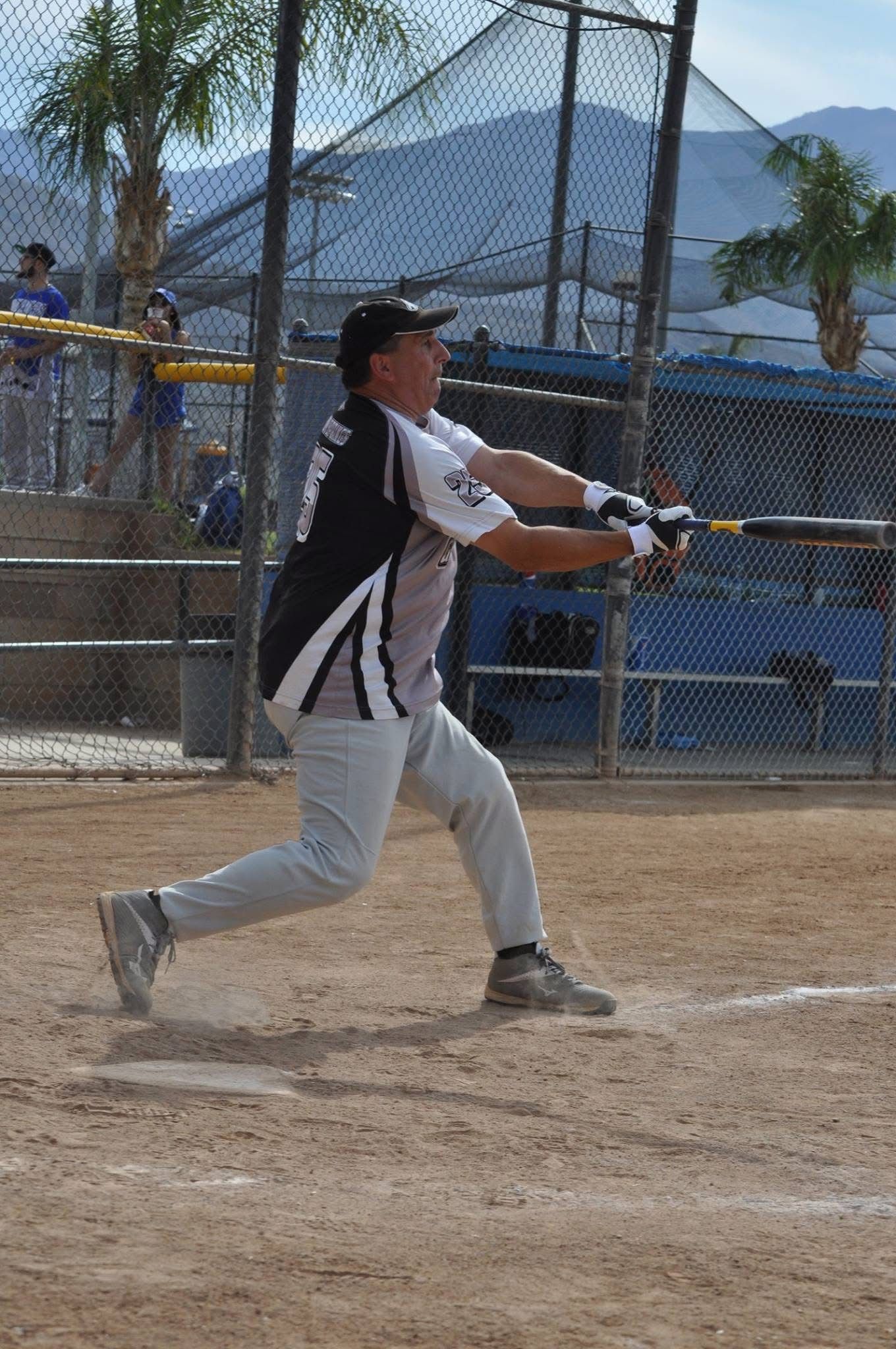 Baseball player in black and white swings a bat on a dirt field with mountains in the background