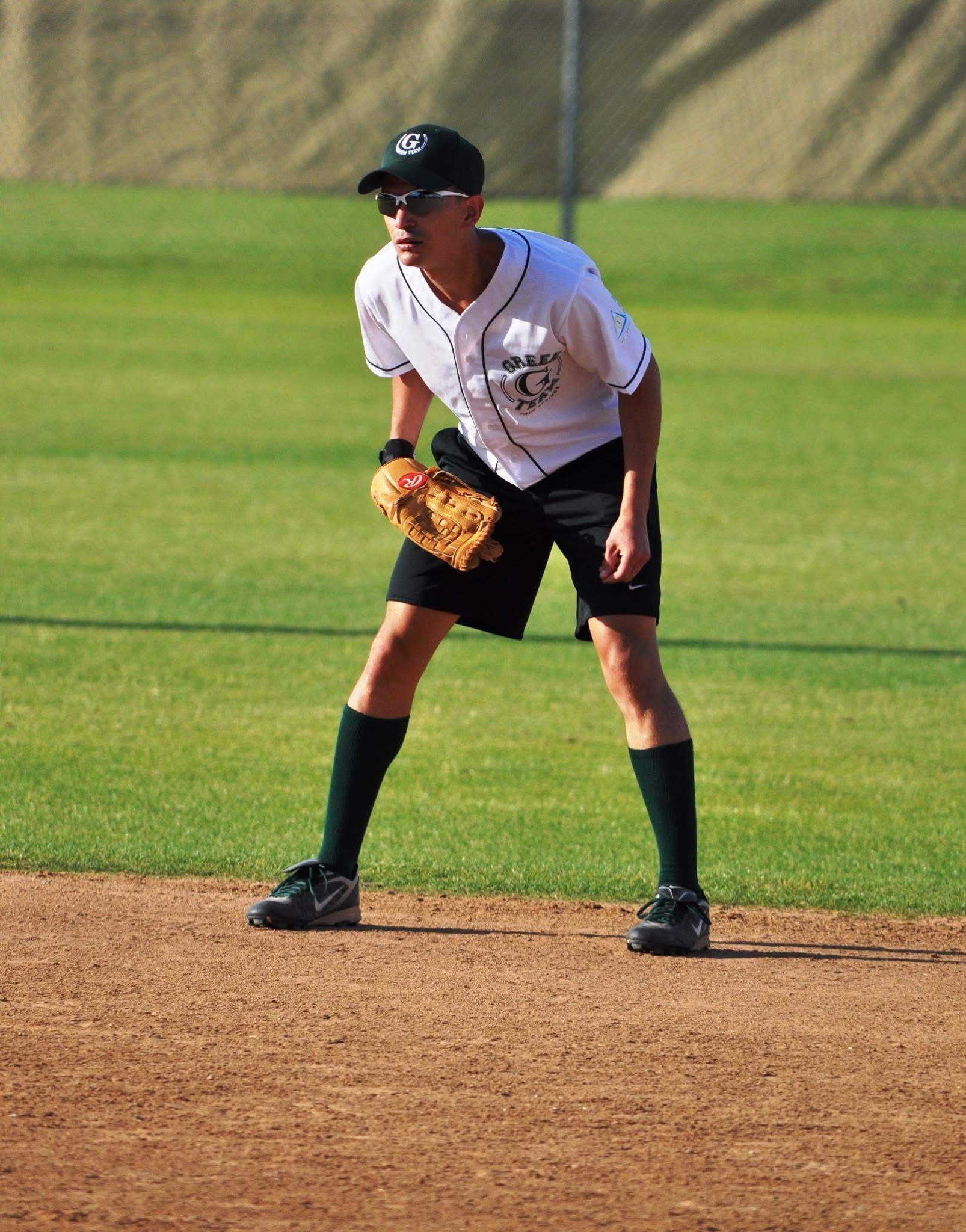 Baseball infielder in white uniform and black cap crouches ready on a dirt infield.