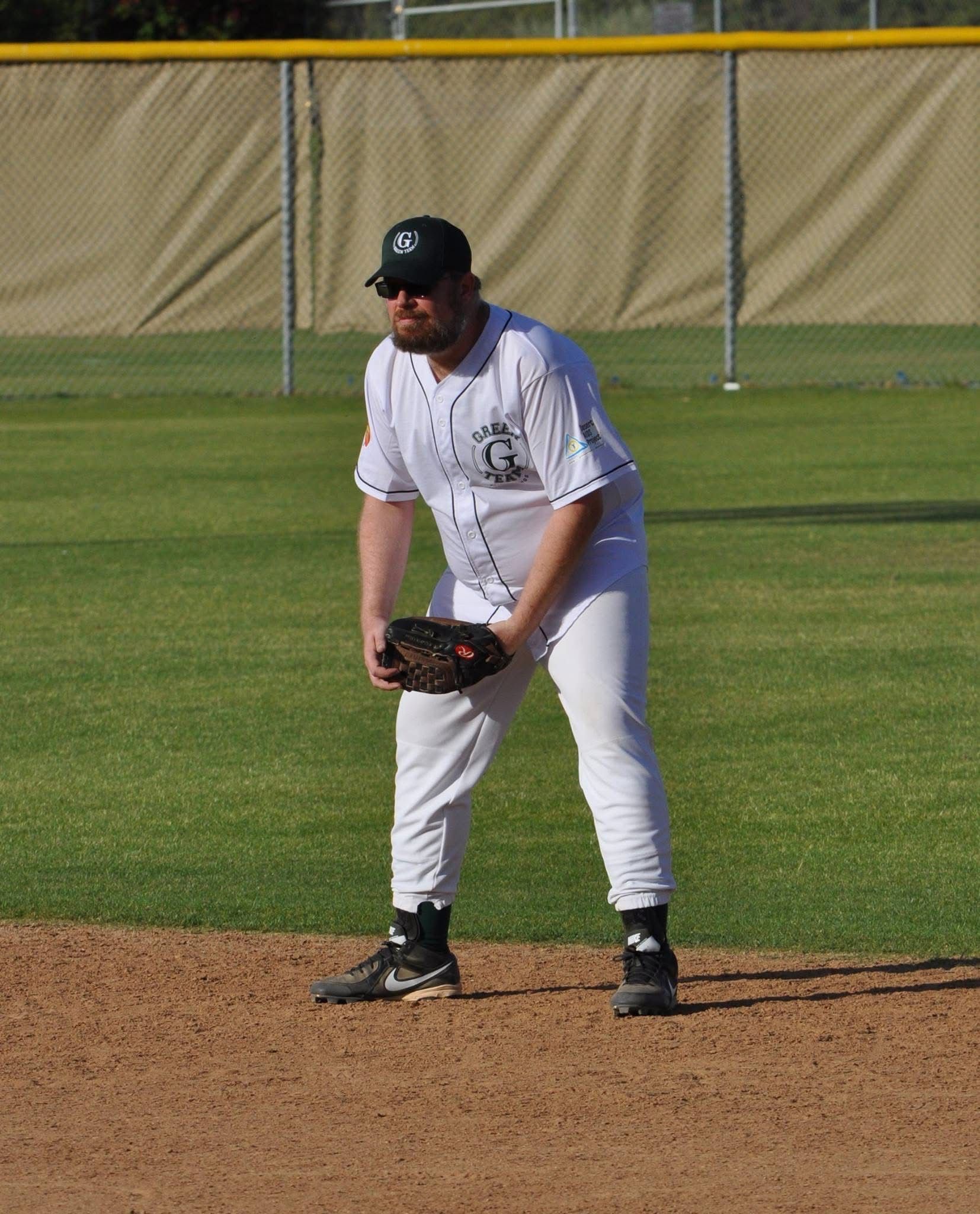 Baseball player in white uniform and black cap fielding a ball on the infield.