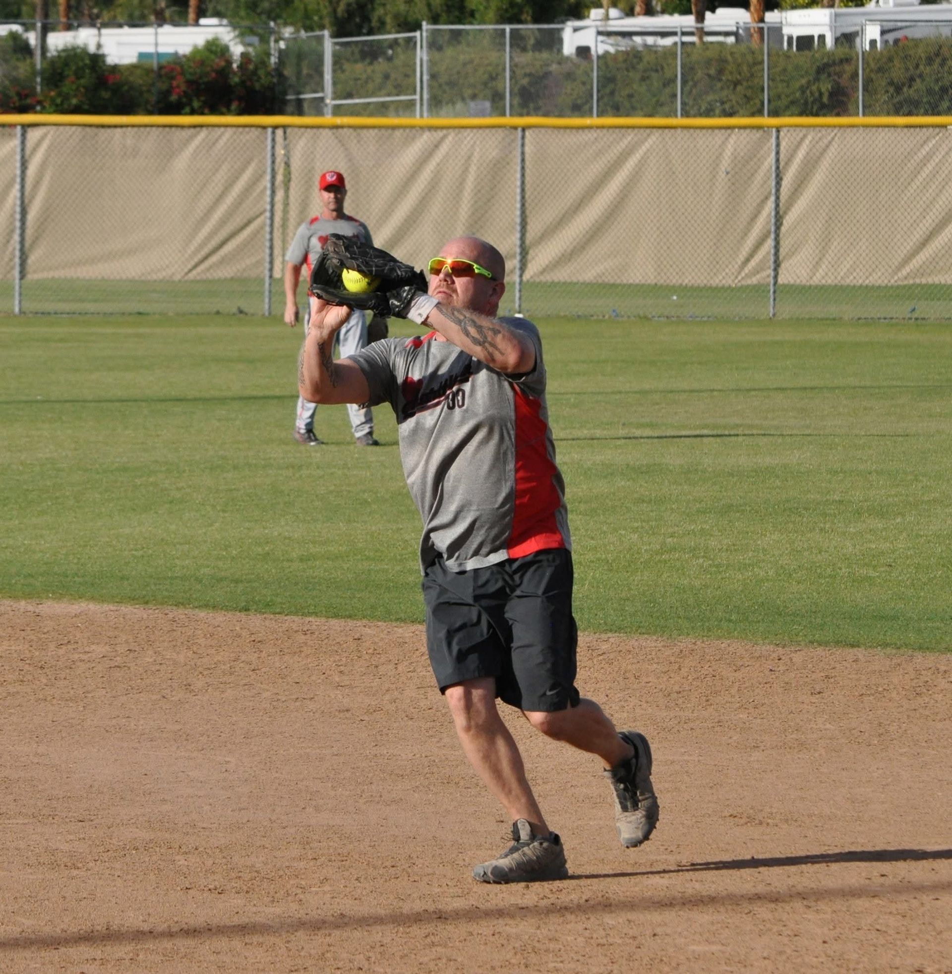 Baseball player in gray and black catches a ball on a dirt infield, with a fielder in the background.