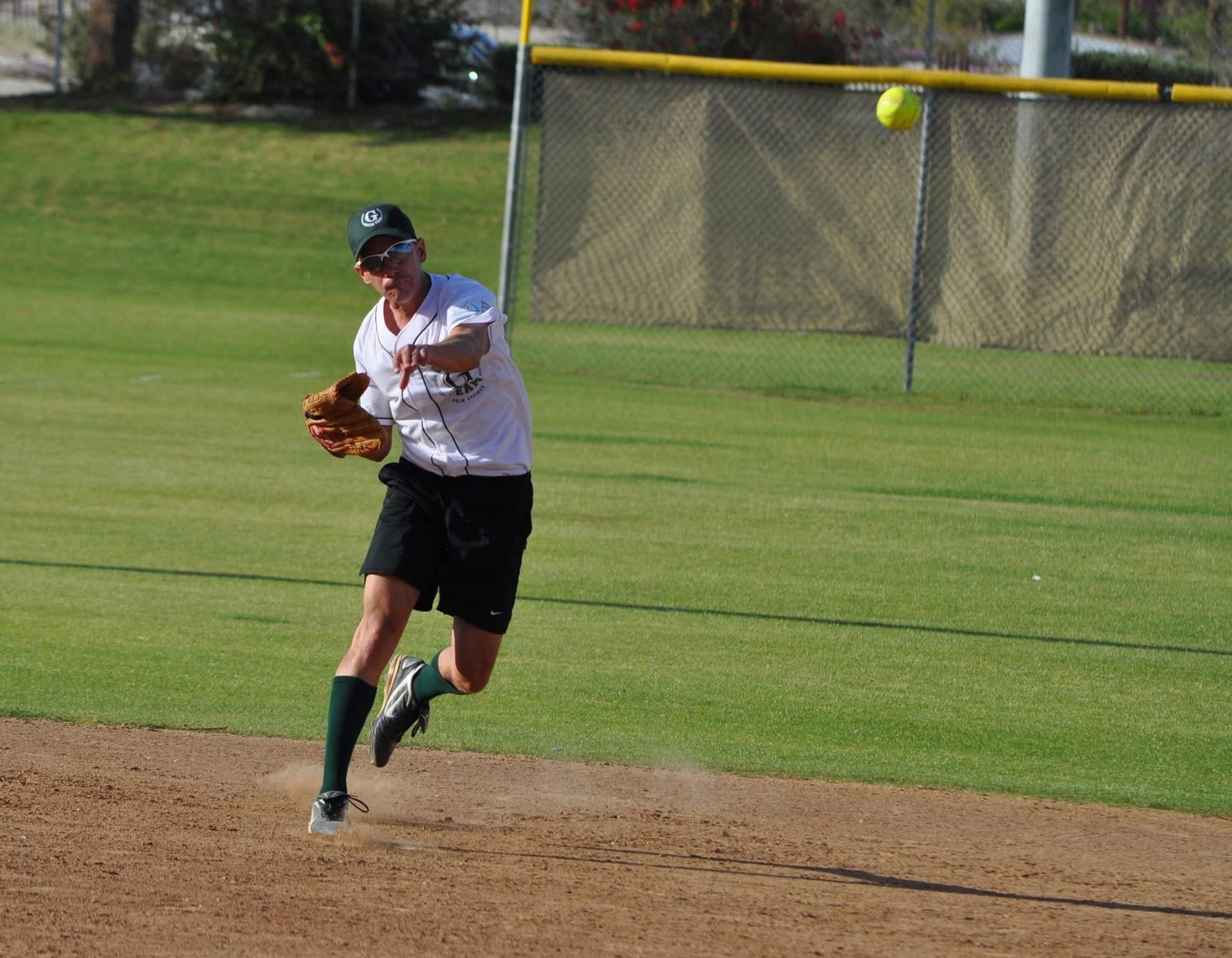 Softball player in white and black uniform fielding a ball on the infield