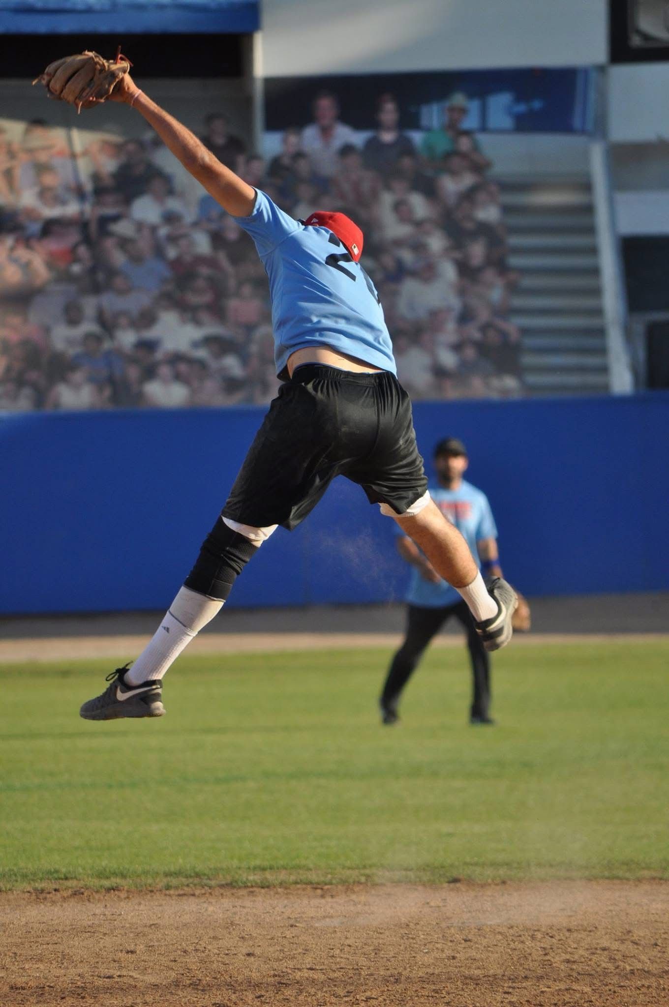 Baseball player in blue leaps for a high catch on the field with a stadium crowd in the background