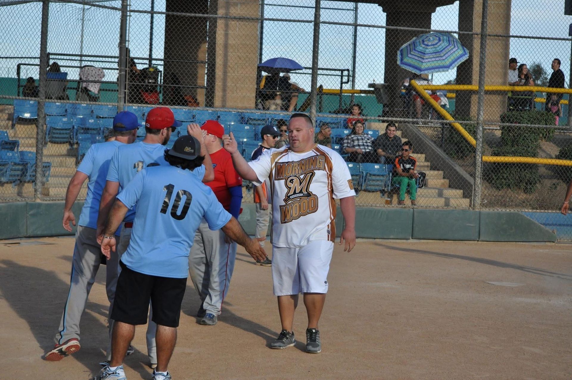 People in blue and red shirts greeting on a softball field near the dugout