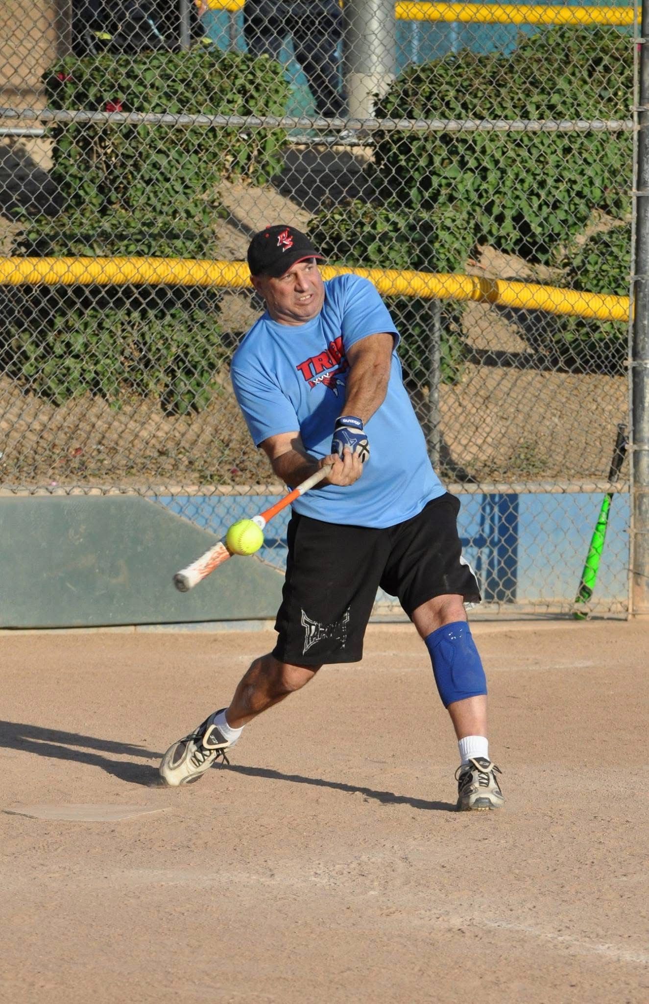 Softball player in blue shirt swings at a pitch on a dirt field