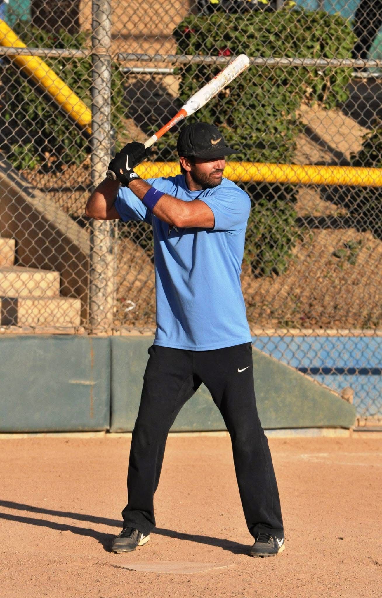 Baseball player in blue shirt and black pants holding a bat in a batting stance on a dirt field
