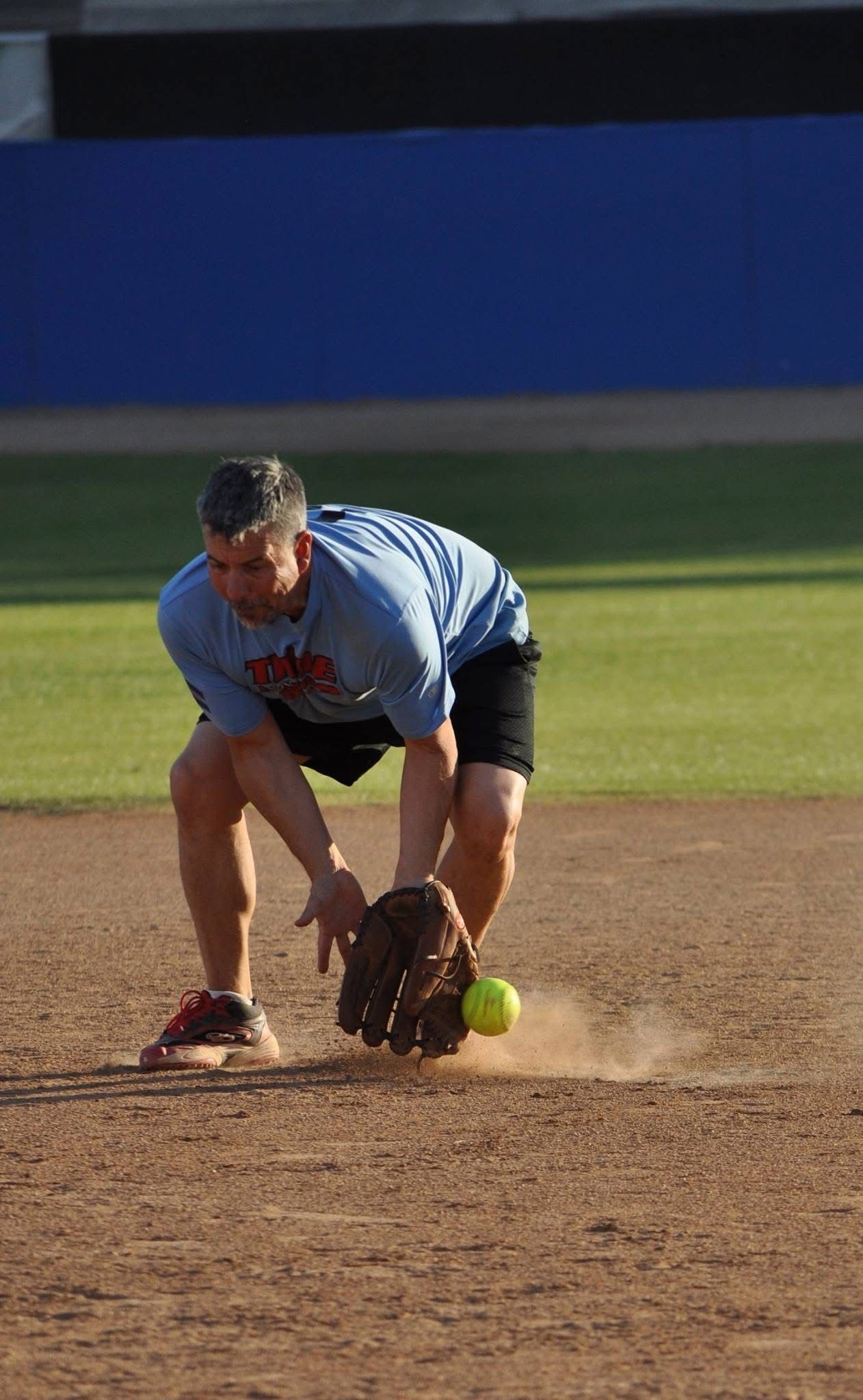 Softball player in blue jersey fields a ground ball on the infield dirt.