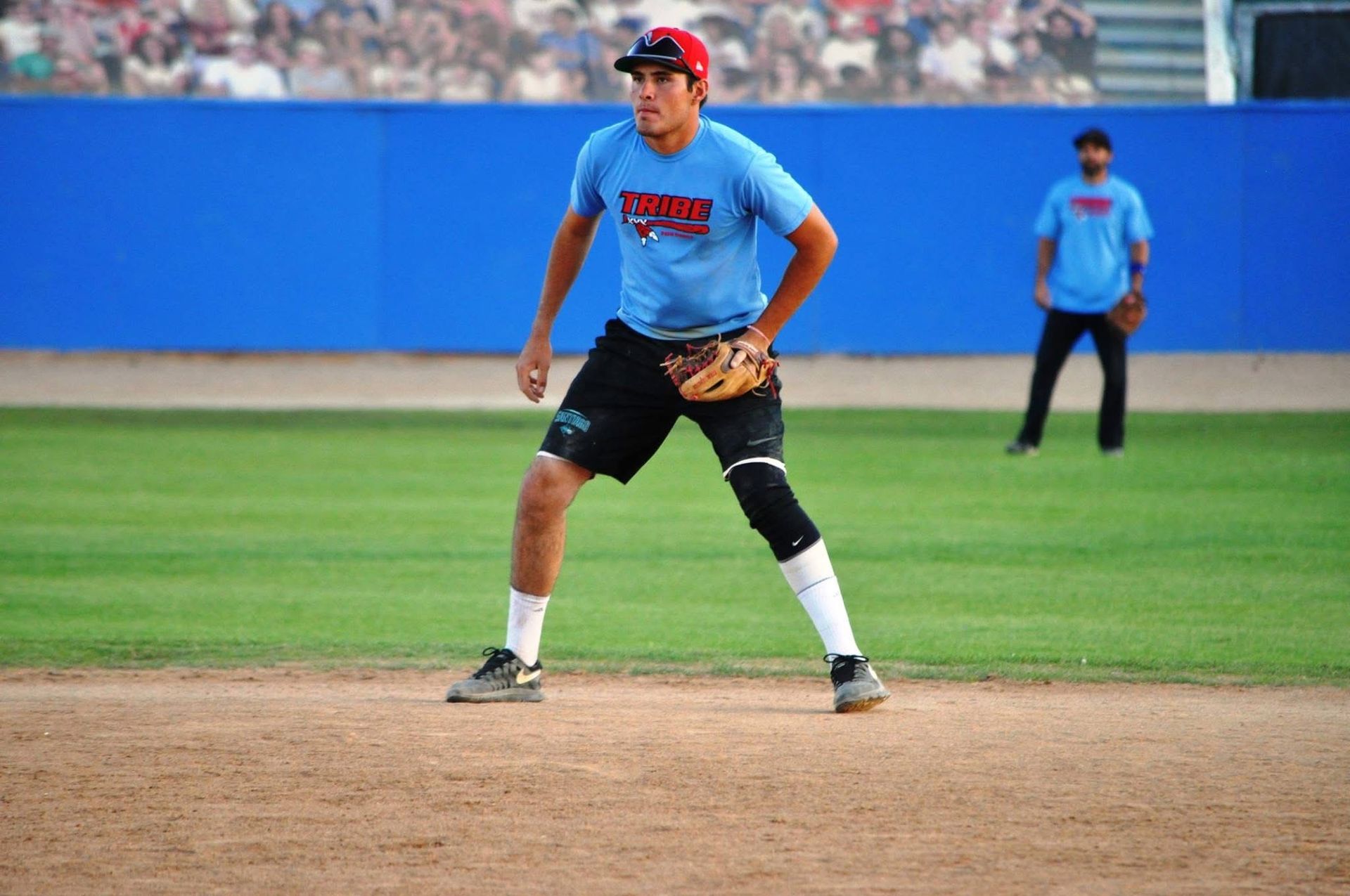Baseball player in blue uniform and black knee brace stands ready on the infield.