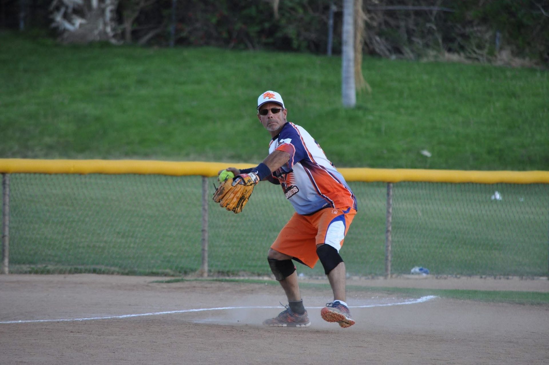 Baseball player in orange and navy uniform fielding a ball near home plate on a dirt field