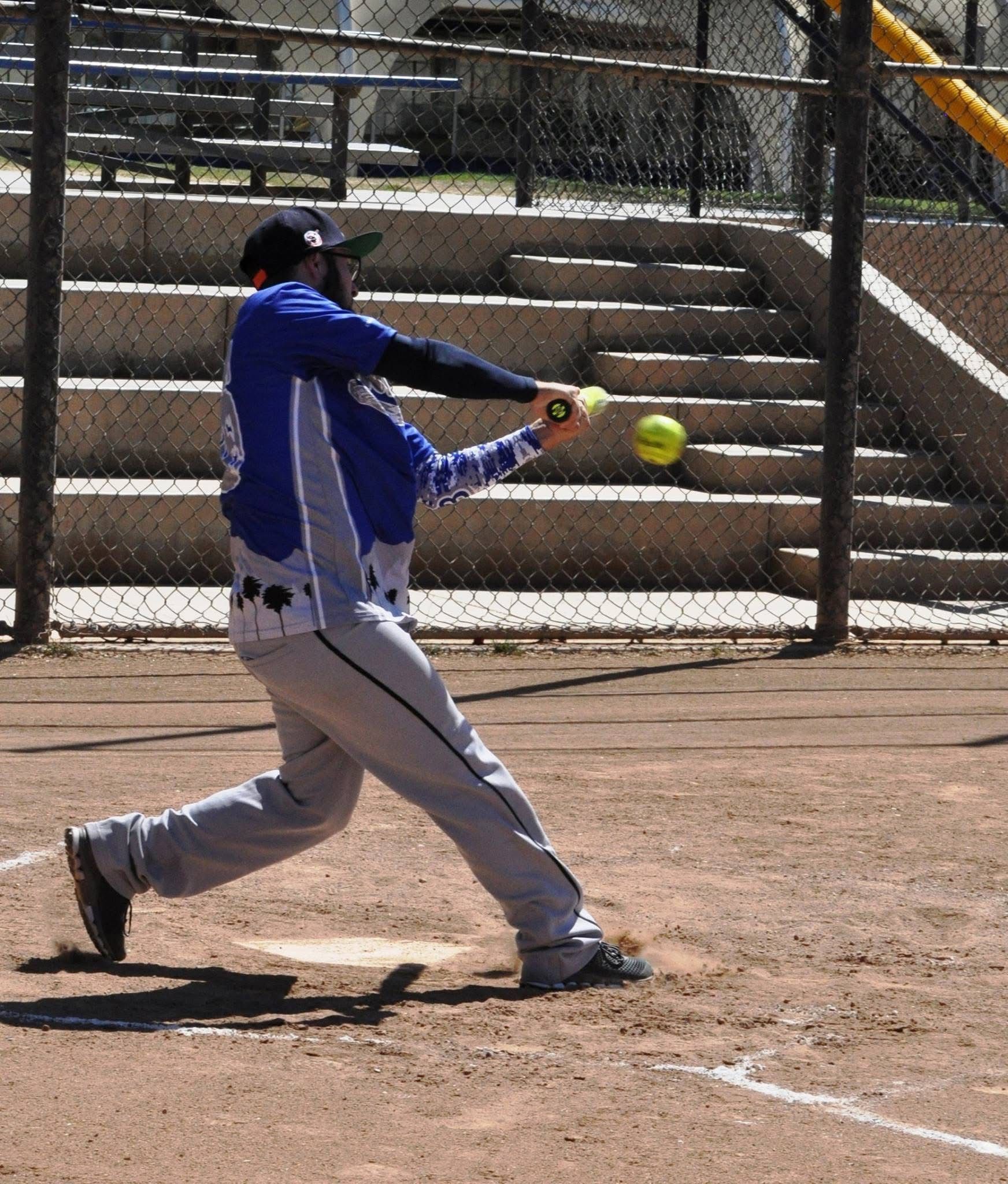 Softball player in blue uniform swinging at a pitched ball on a dirt field
