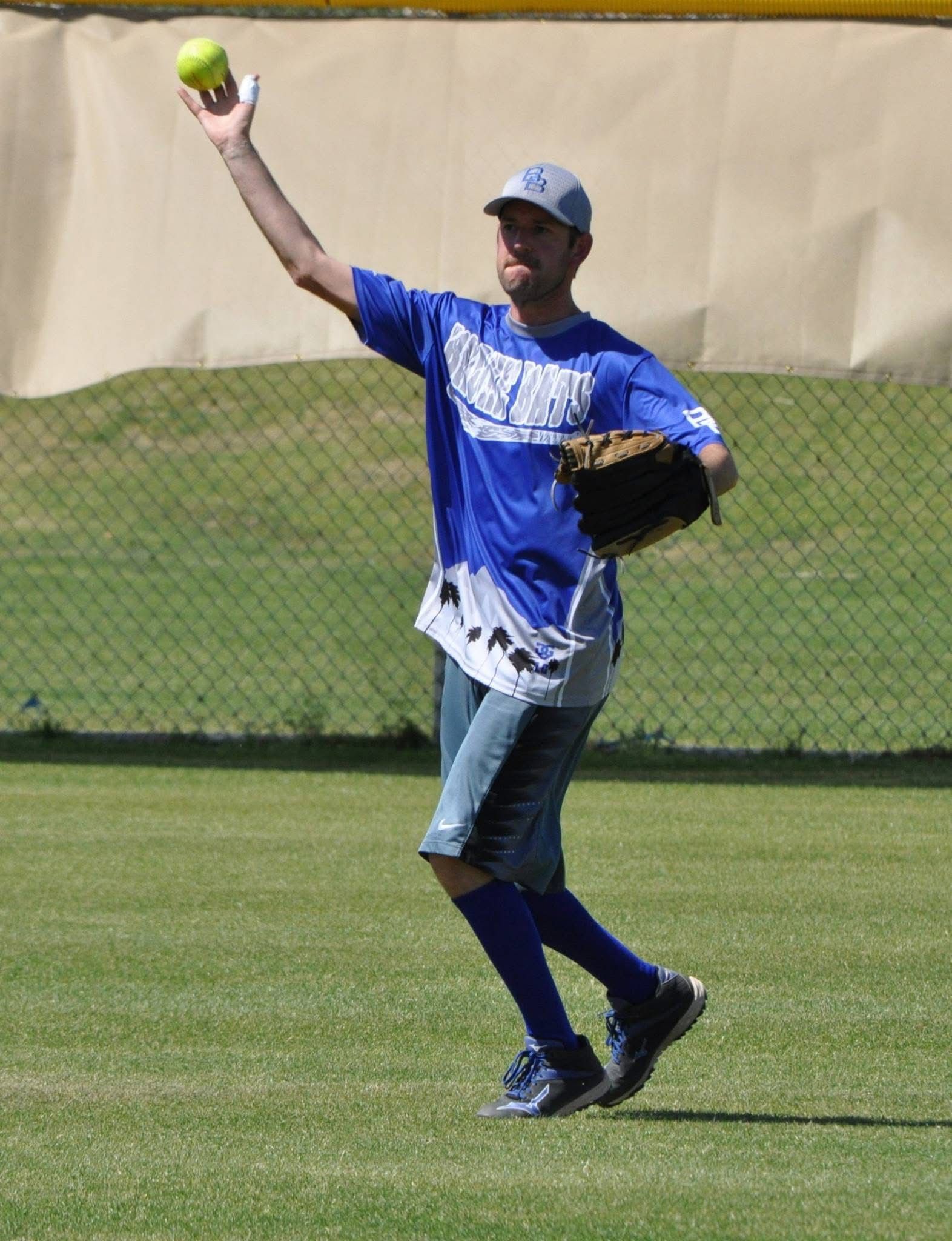 Softball player in blue uniform mid-throw on a field, holding a ball with glove ready